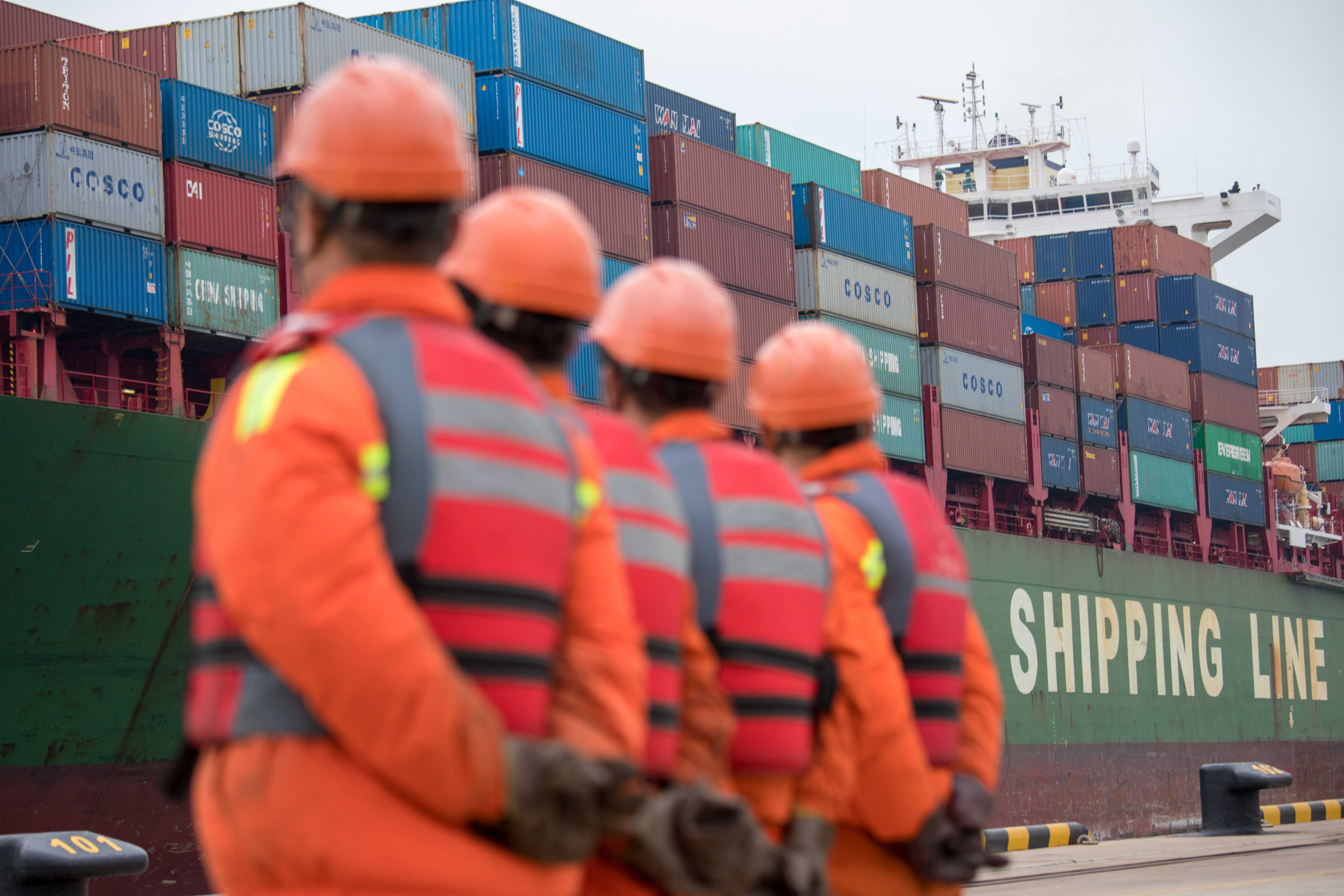 Workers look on as a cargo ship approaches a terminal at the port of Qingdao in Shandong