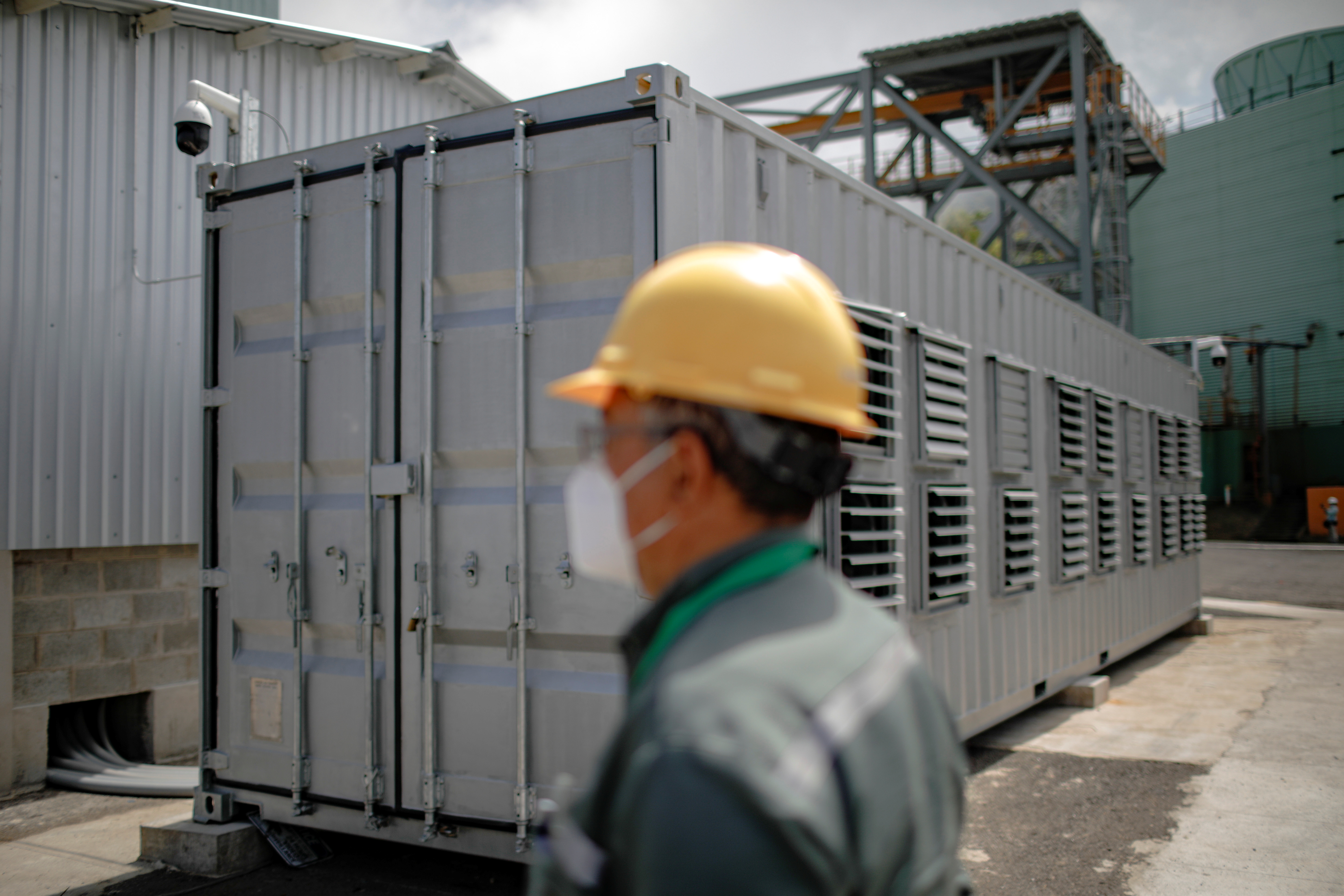 A worker is seen next to a container, where a Bitcoin mining facility is installed, at the Berlin geothermal plant of La Geo electrical company, in Alegria
