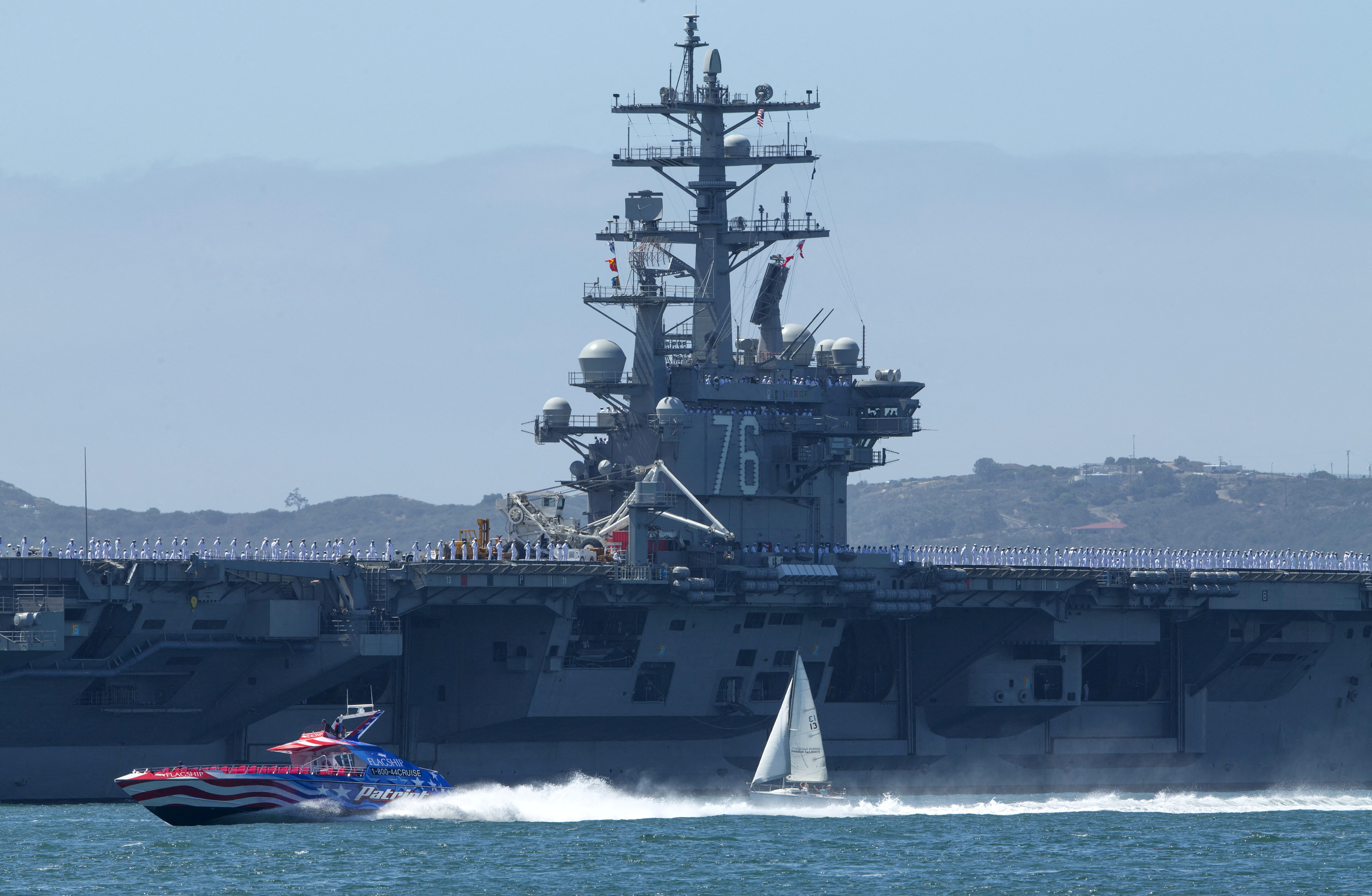 A speed boat and a sail boat pass as the USS Ronald Reagan, departs for Yokosuka, Japan from Naval Station North Island in San Diego