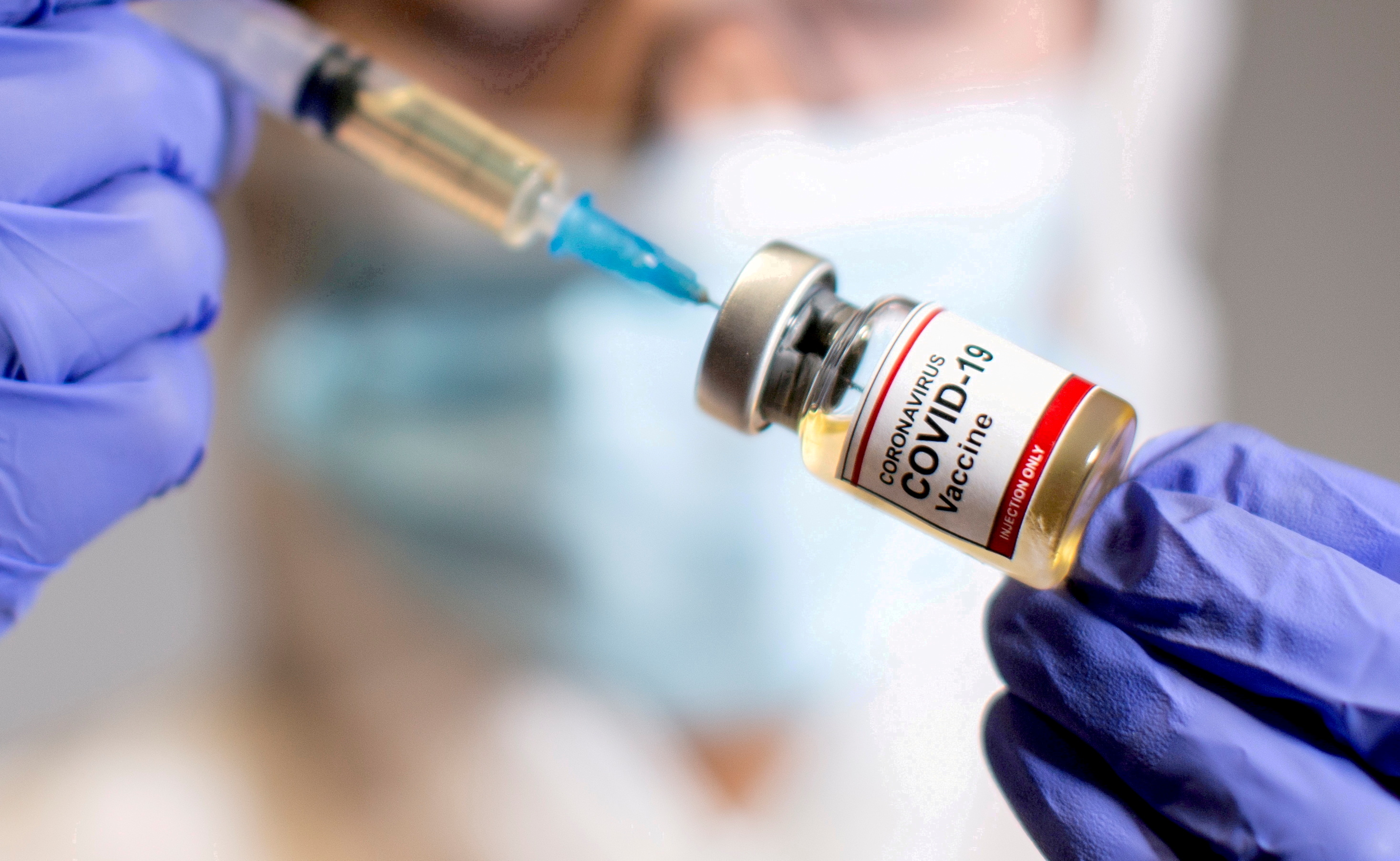 A woman holds a medical syringe and a small bottle labelled "Coronavirus COVID-19 Vaccine