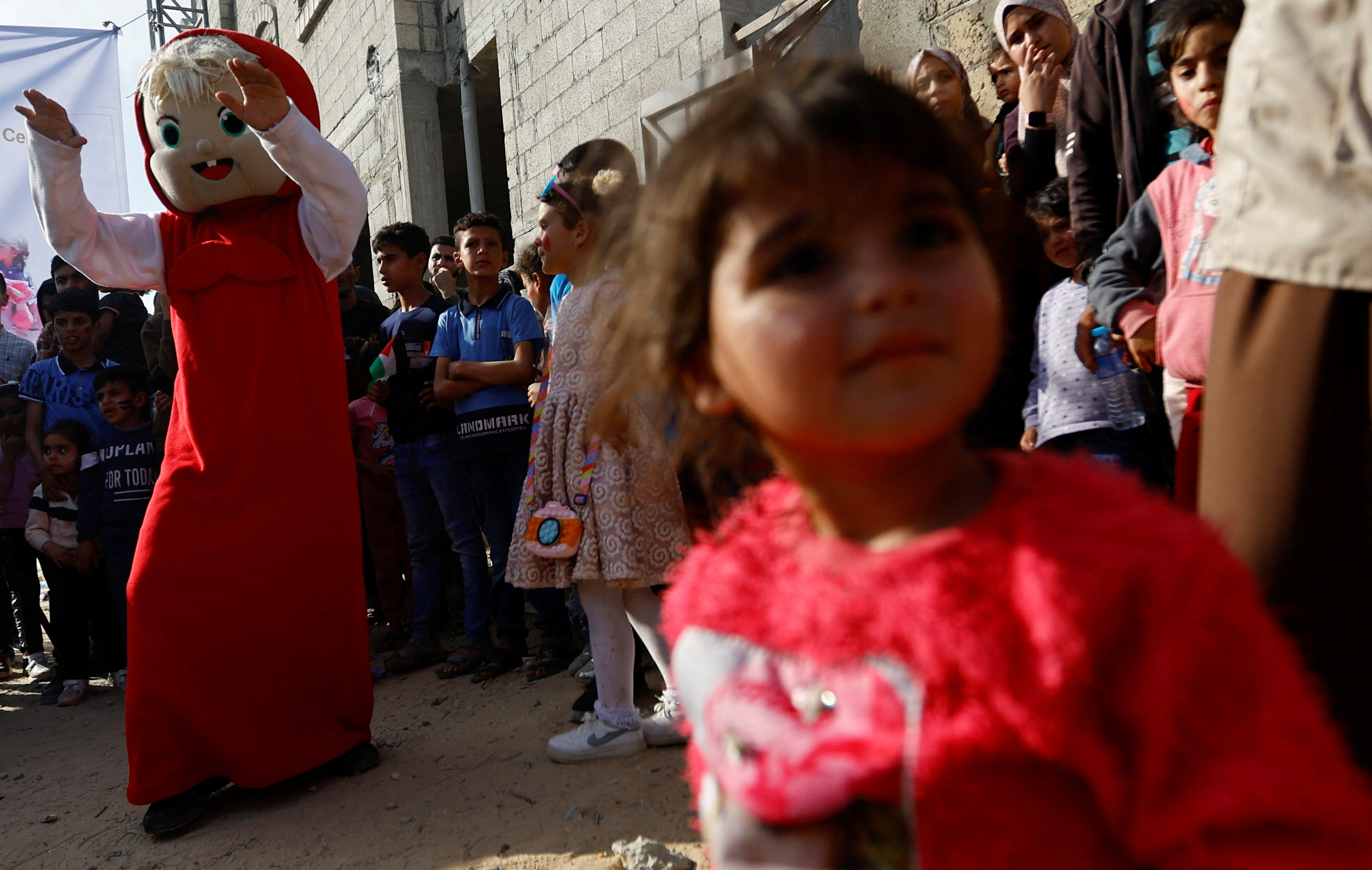 A girl looks on as a Palestinian dressed in a costume entertains children in Deir al-Balah