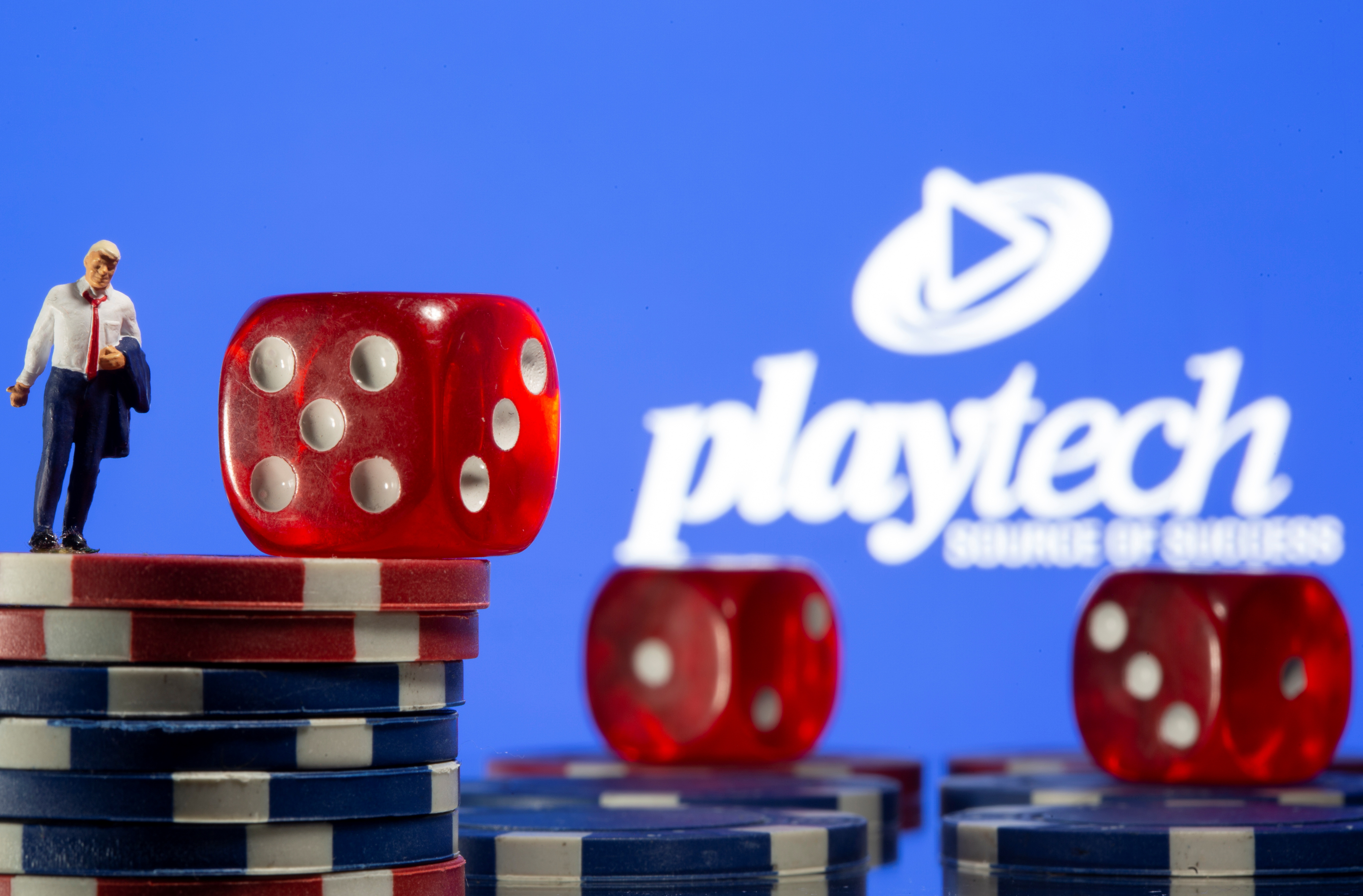 Businessman toy figure is placed on gambling chips in front of displayed Playtech logo in this illustration taken