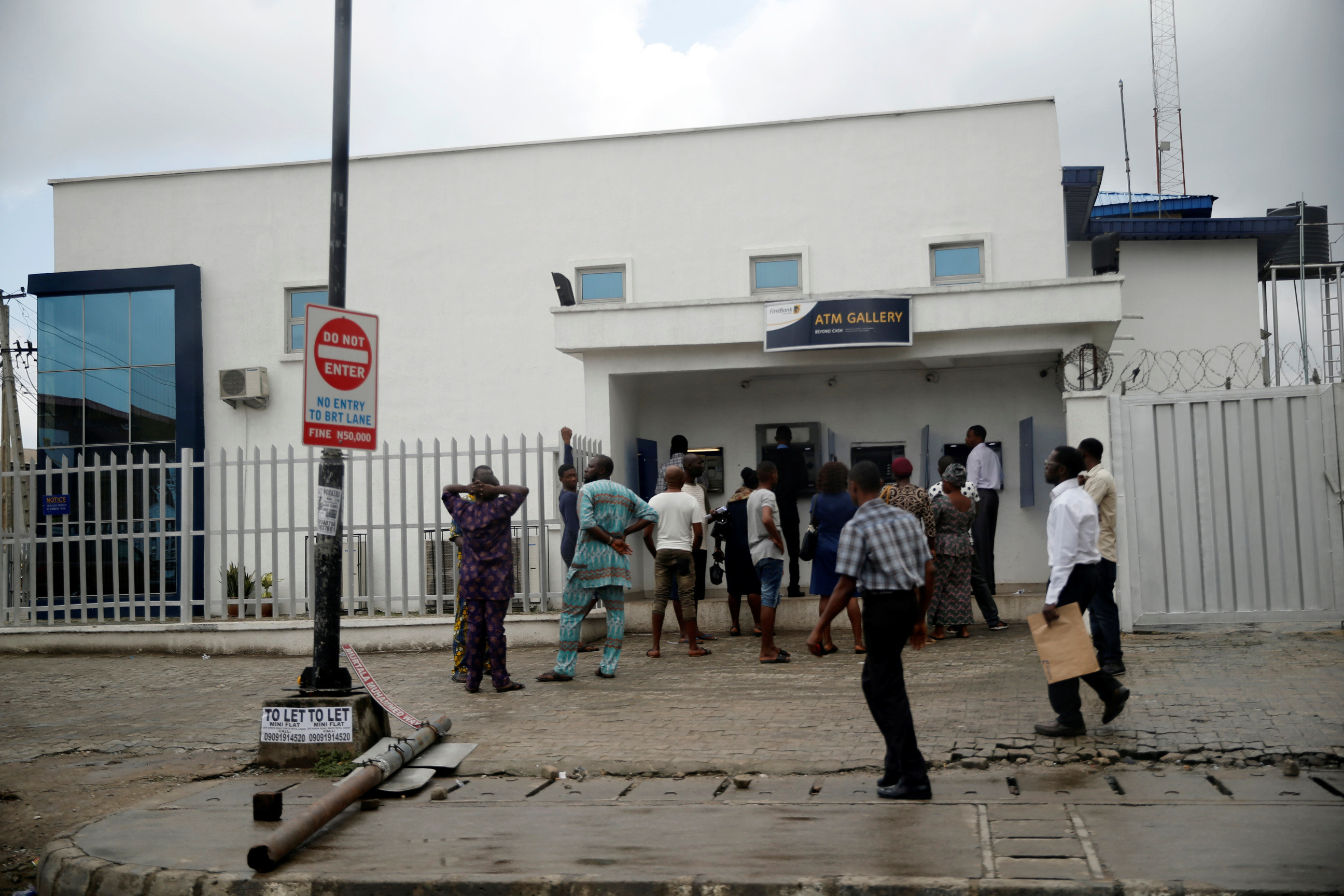 People queue to use the automated teller machine (ATM) in front of First bank along a road in Apapa district in Lagos
