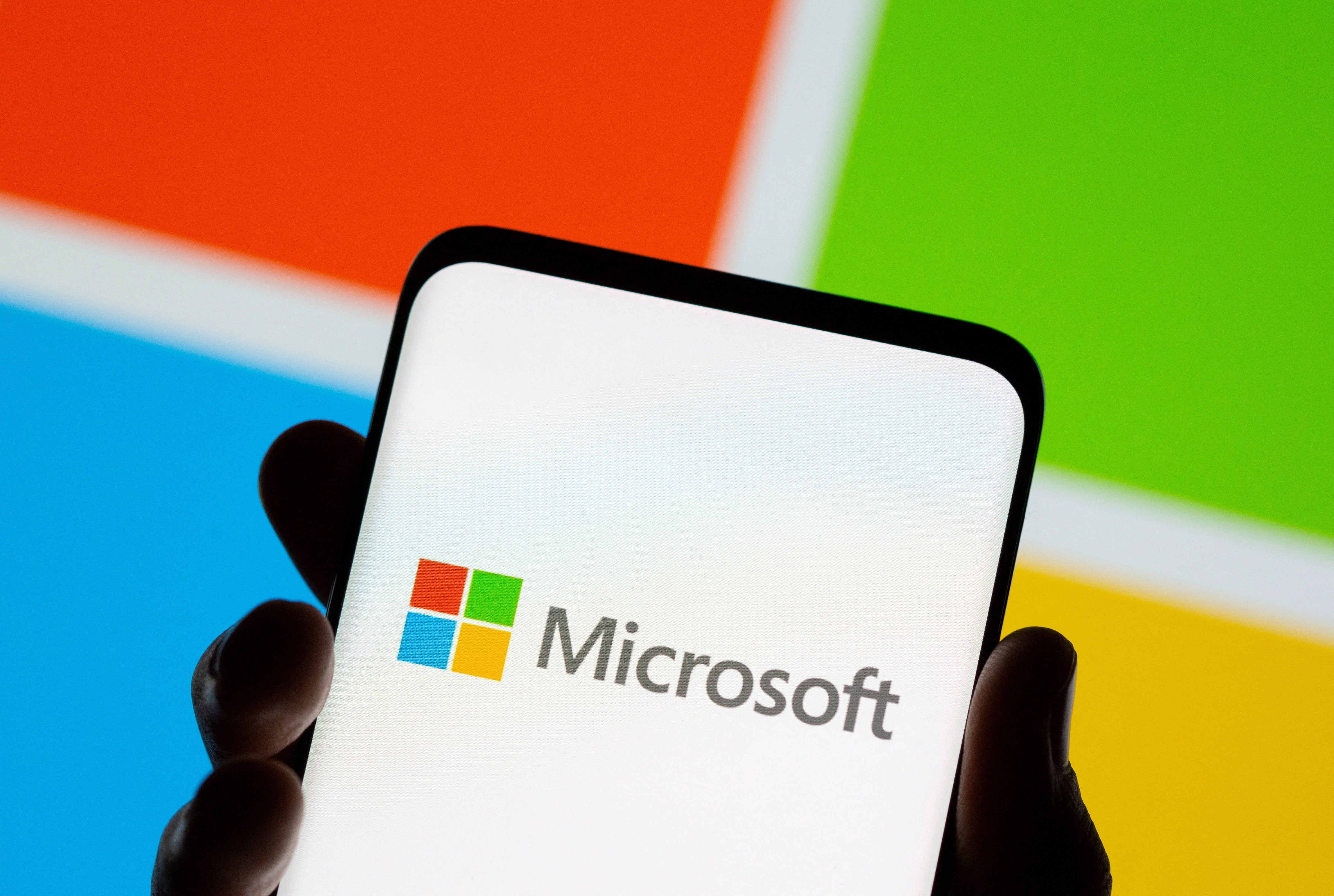 Smartphone is seen in front of Microsoft logo displayed 