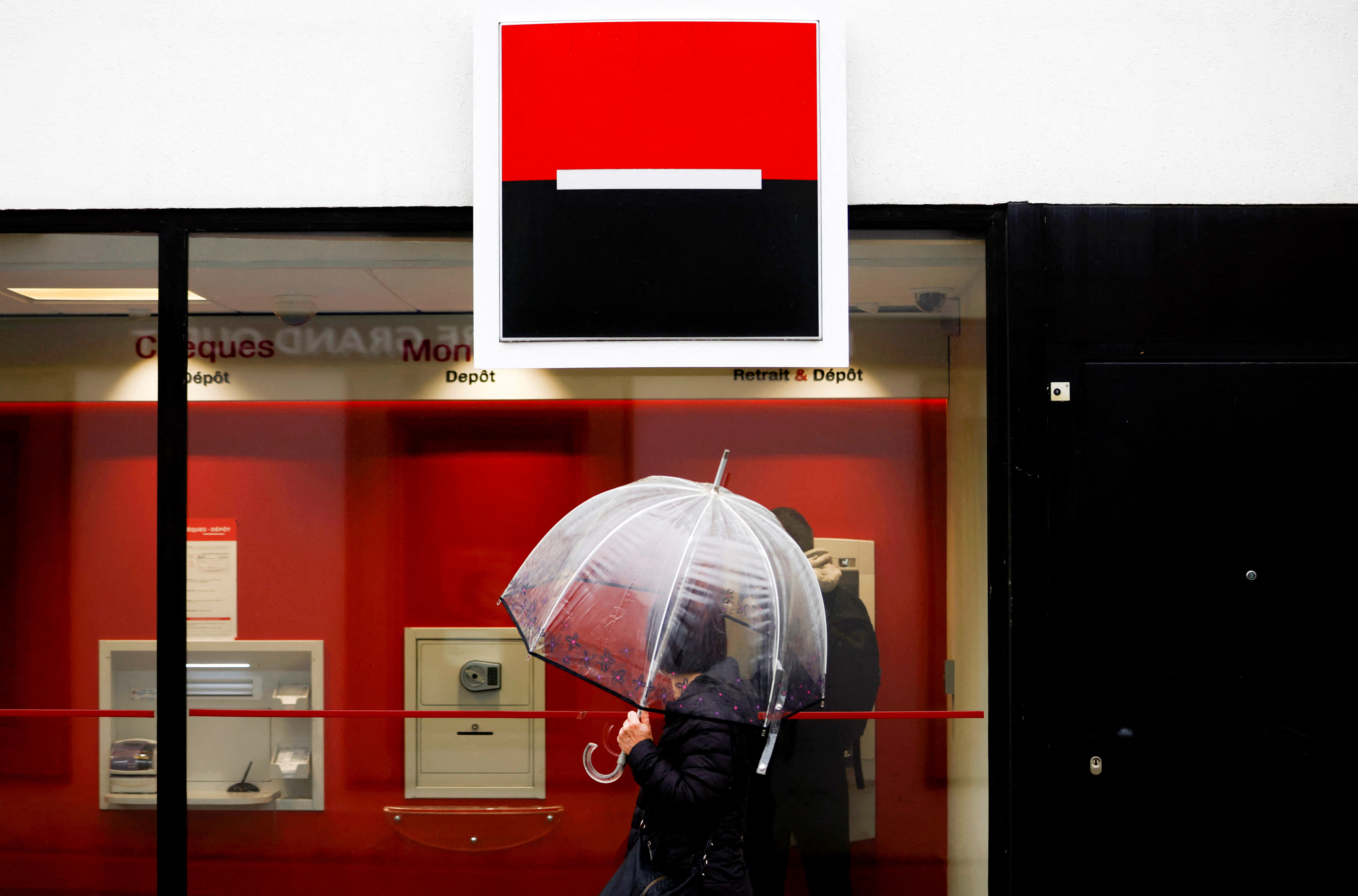 A person holds an umbrella as the logo of French Bank Societe Generale is seen outside a bank building in Saint-Sebastien-sur-Loire near Nantes