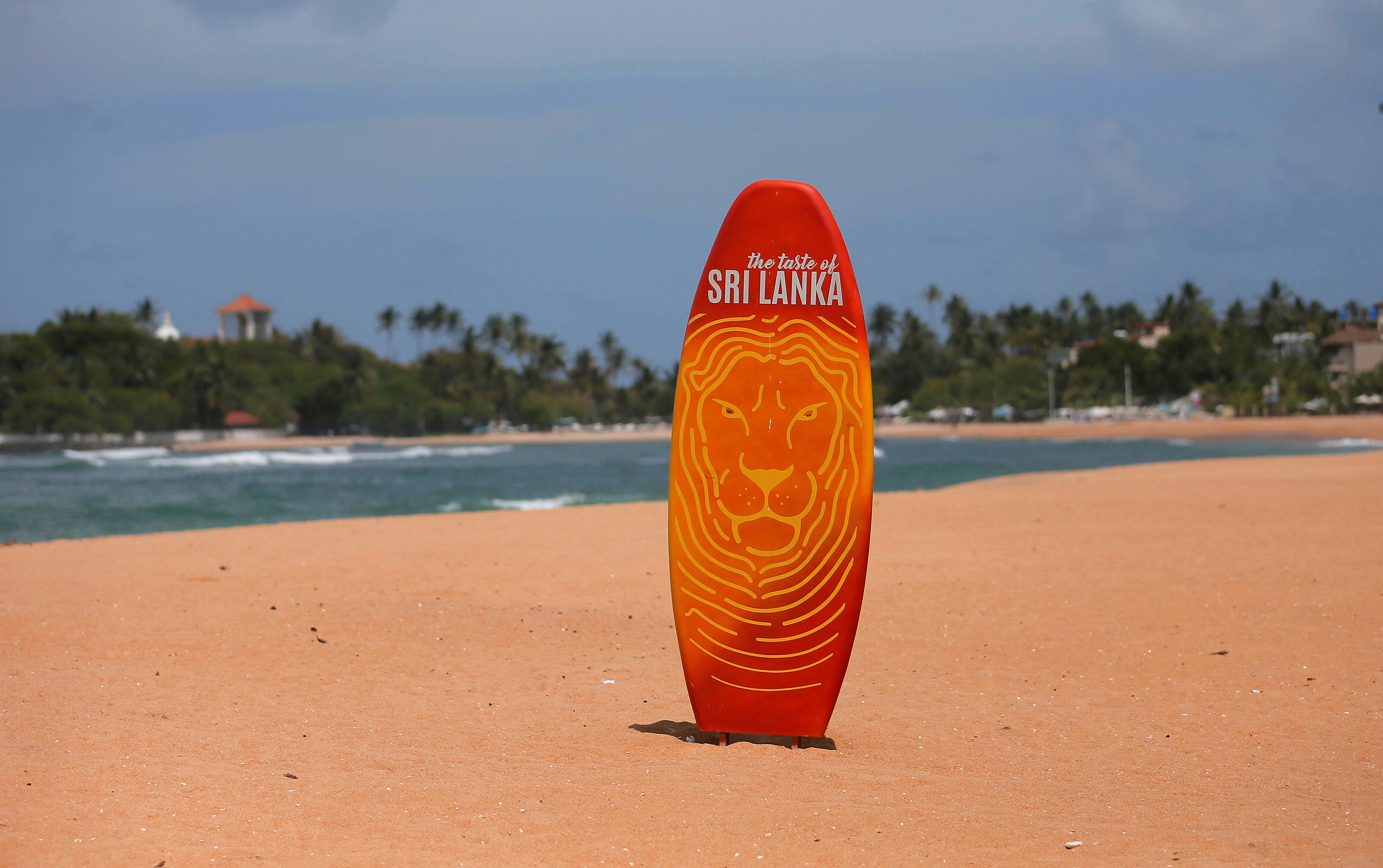 A surfboard is seen in the middle of an empty beach, near hotels at Unawatuna beach in Galle