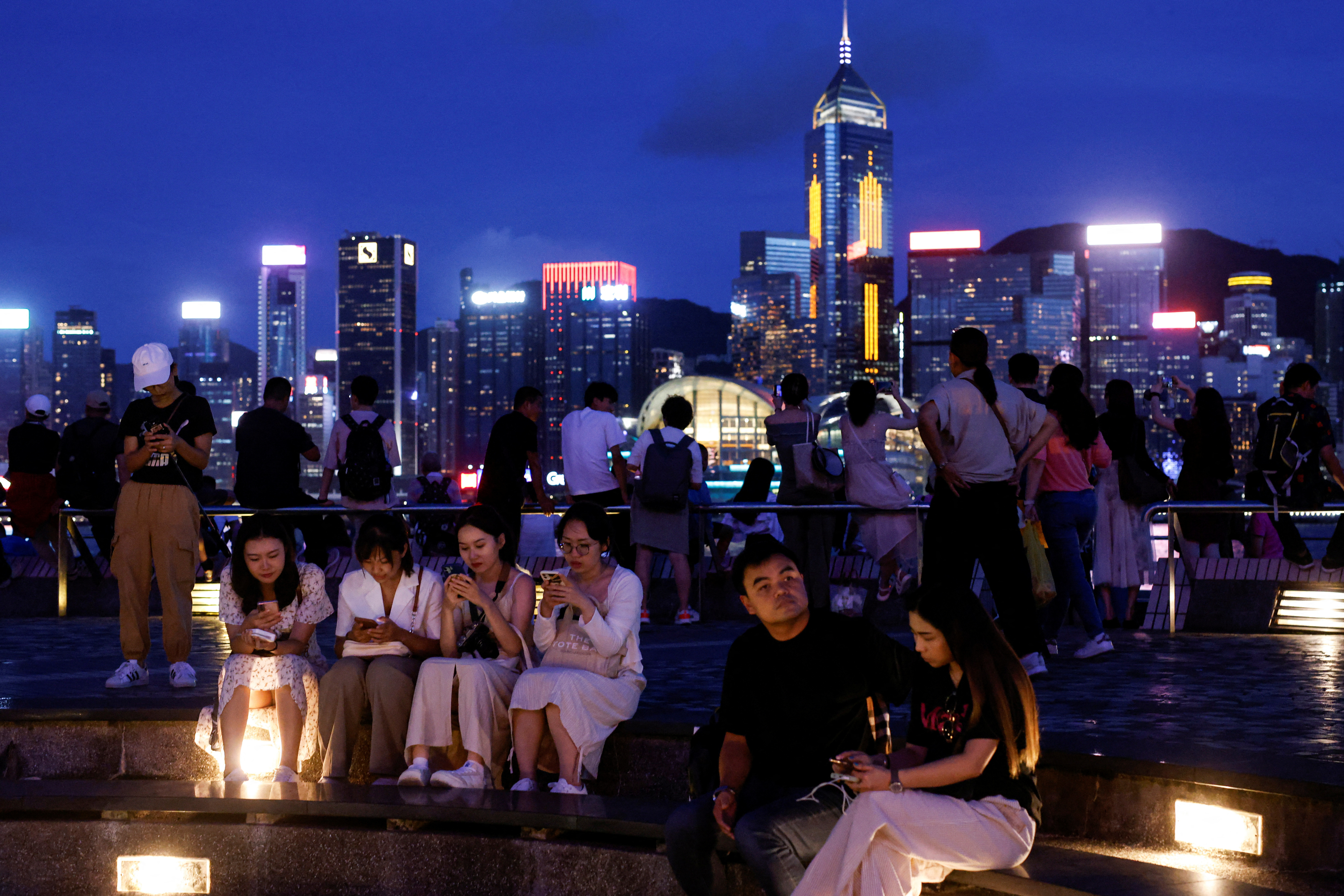 Tourists relax on the waterfront in front of Victoria Harbour, in Hong Kong