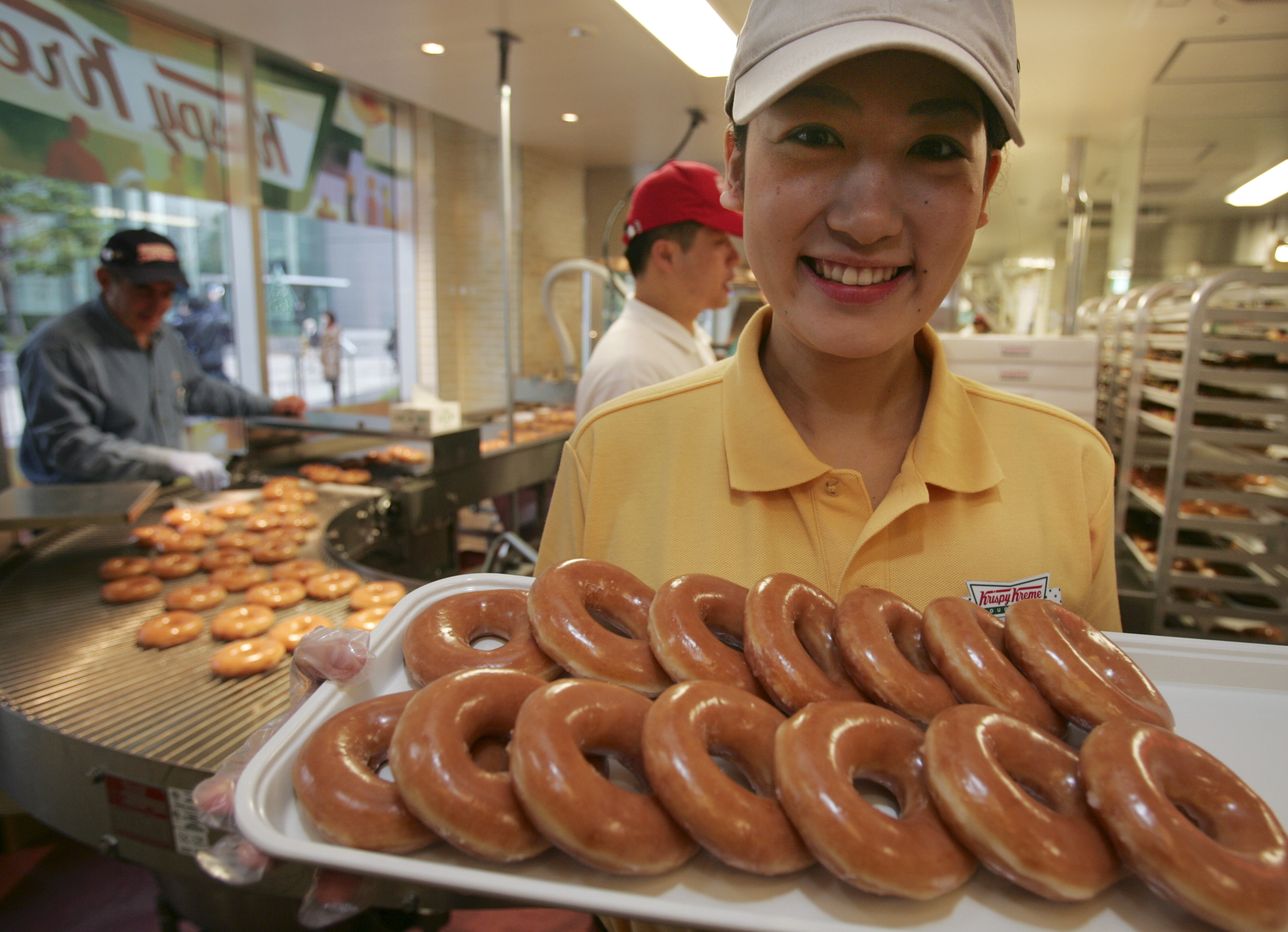 Store attendant poses with a tray of fresh doughnuts at a new Krispy Kreme shop in Tokyo