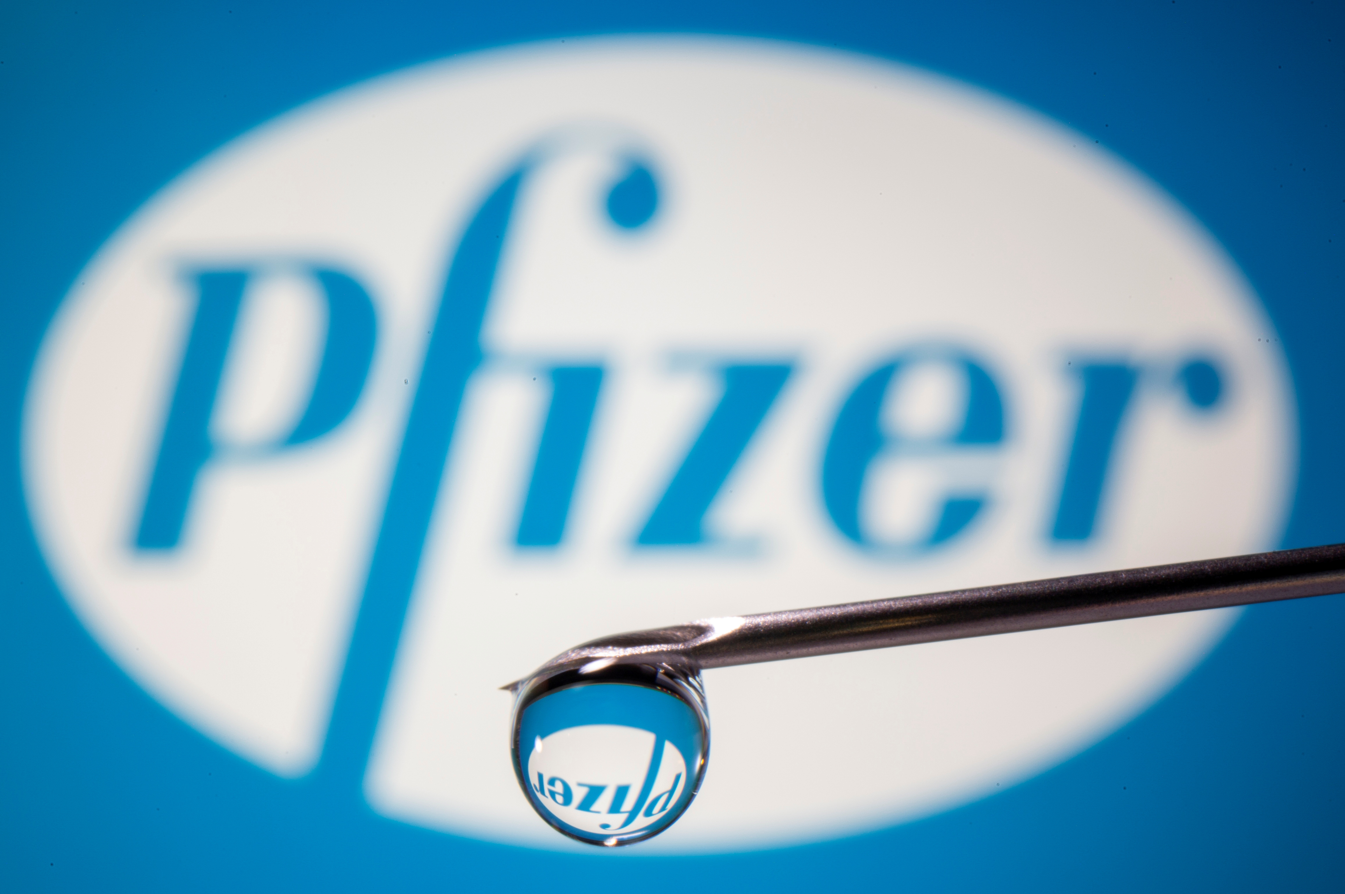 Pfizer's logo is reflected in a drop on a syringe needle in this illustration