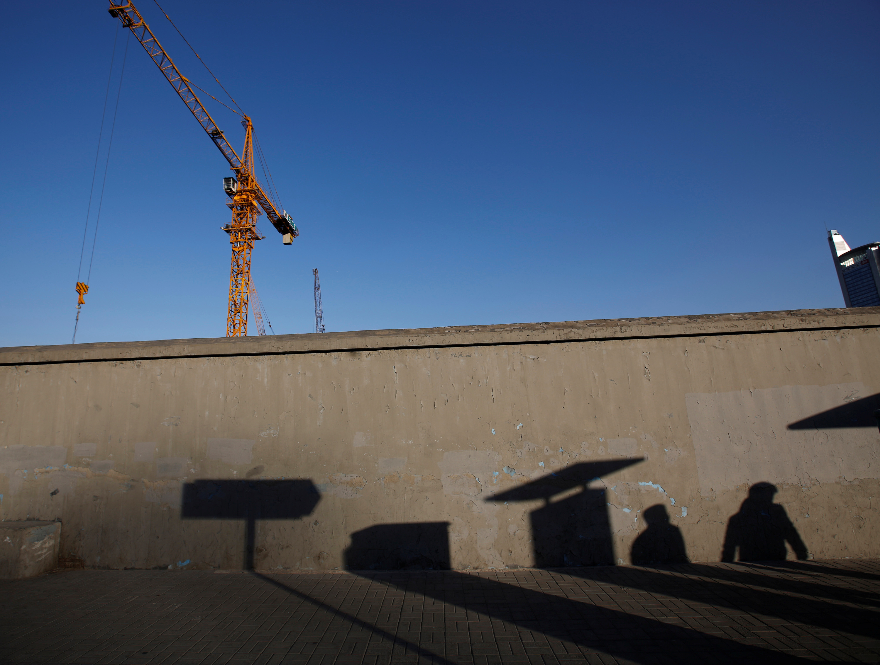 Pedestrians cast their shadows  on a wall at a construction site in Beijing