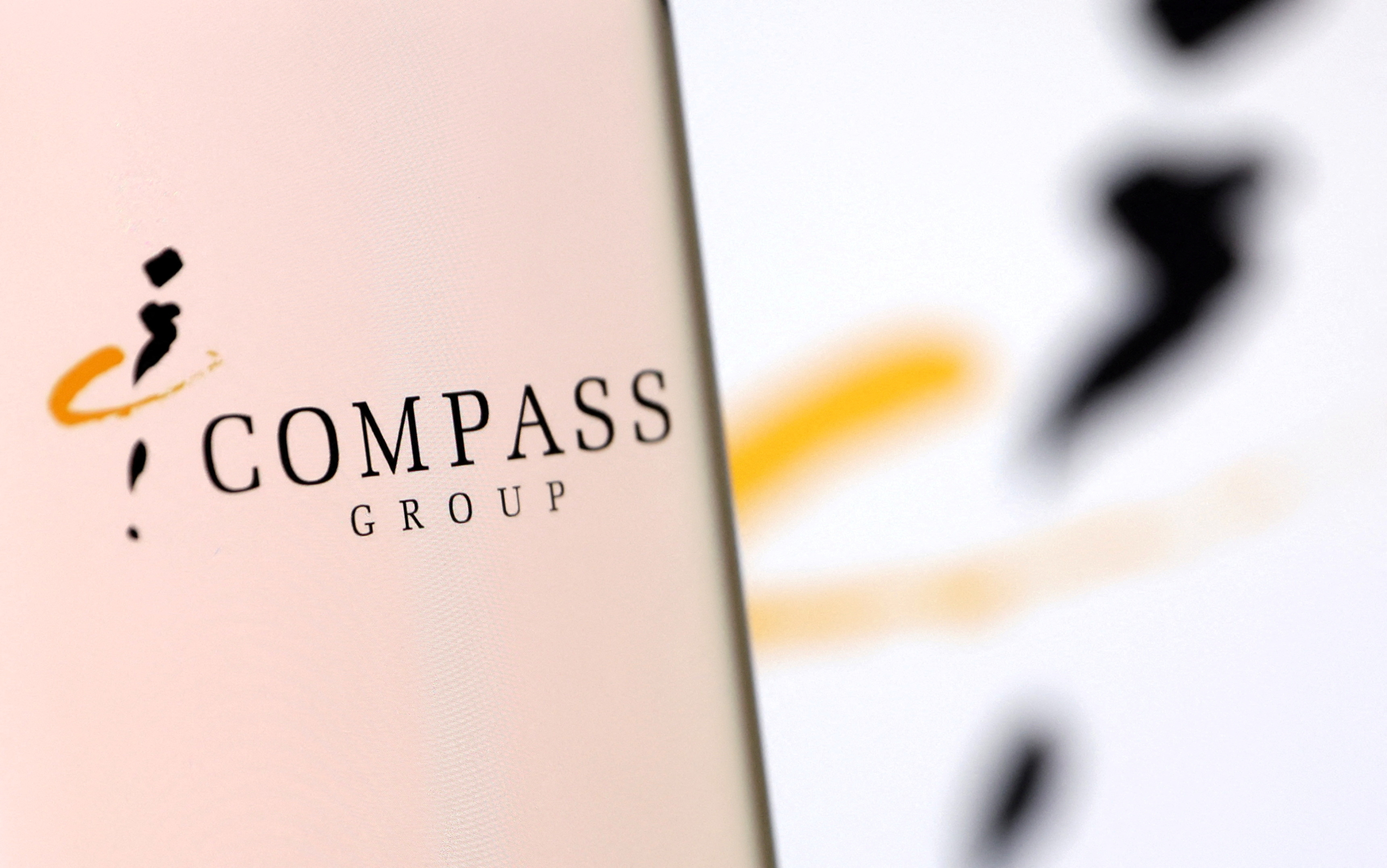 Illustration shows smartphone with Compass Group's logo displayed