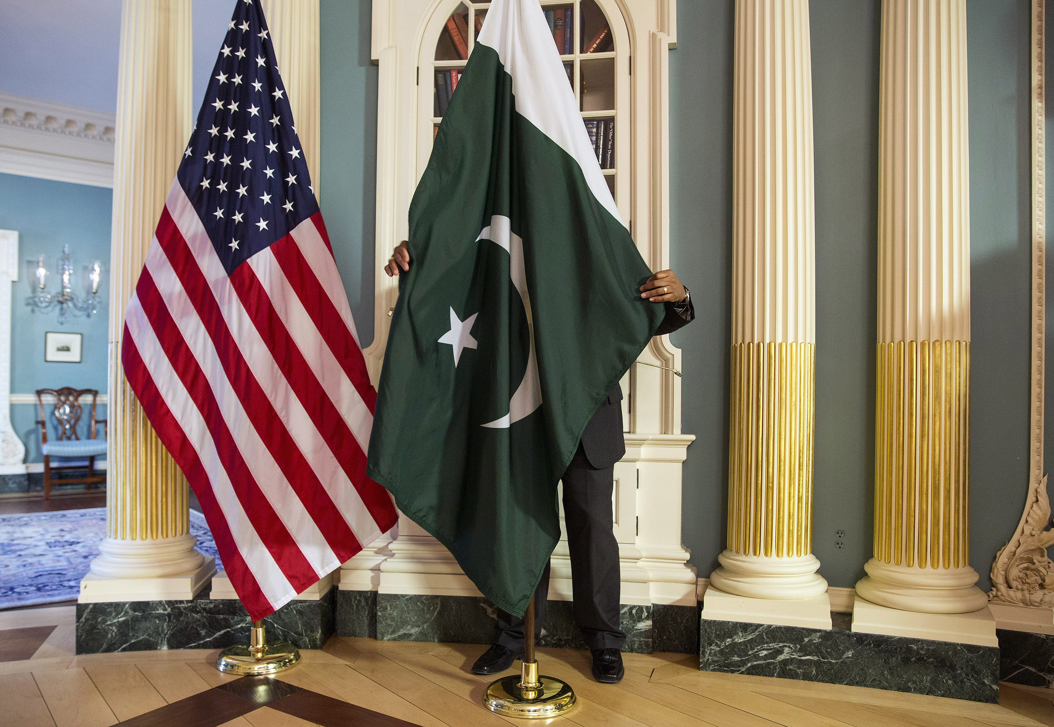 A State Department contractor adjust a flag before a meeting between U.S. Secretary of State Kerry and Pakistan's Interior Minister Khan on the sidelines of the White House Summit on Countering Violent Extremism at the State Department in Washington