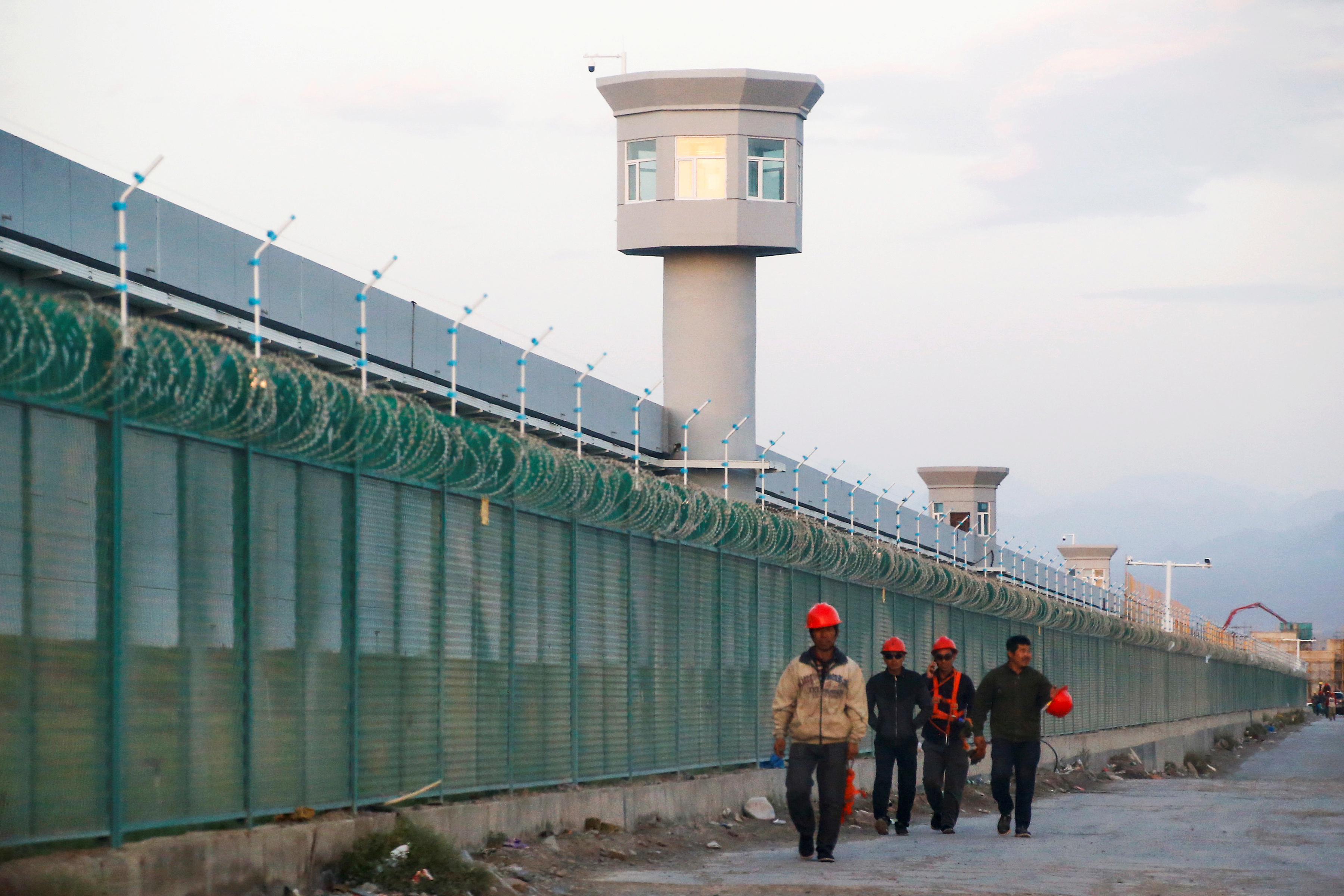 Workers walk by the perimeter fence of what is officially known as a vocational skills education centre in Dabancheng
