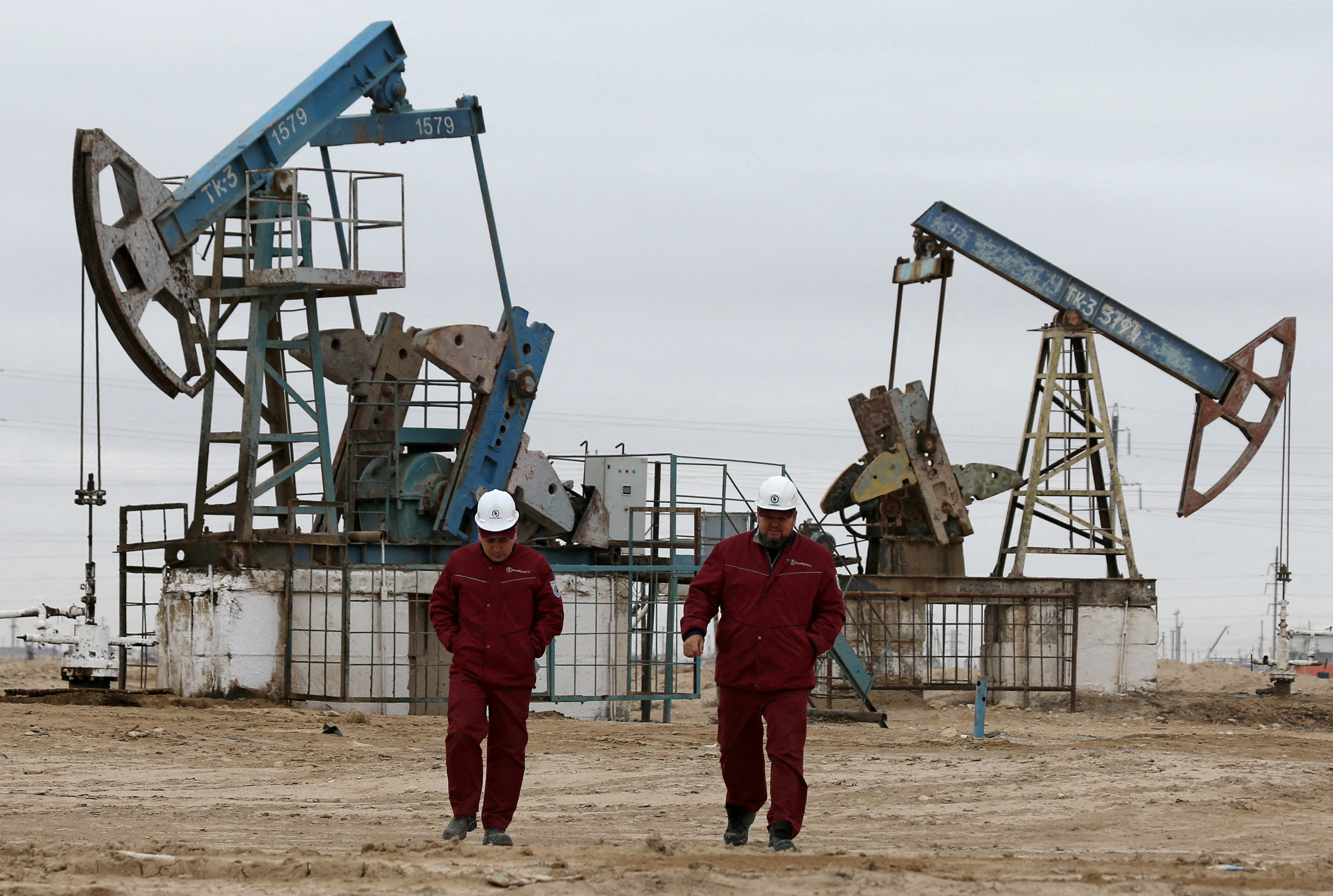 Workers walk as oil pumps are seen in the background in the Uzen oil and gas field in the Mangistau Region