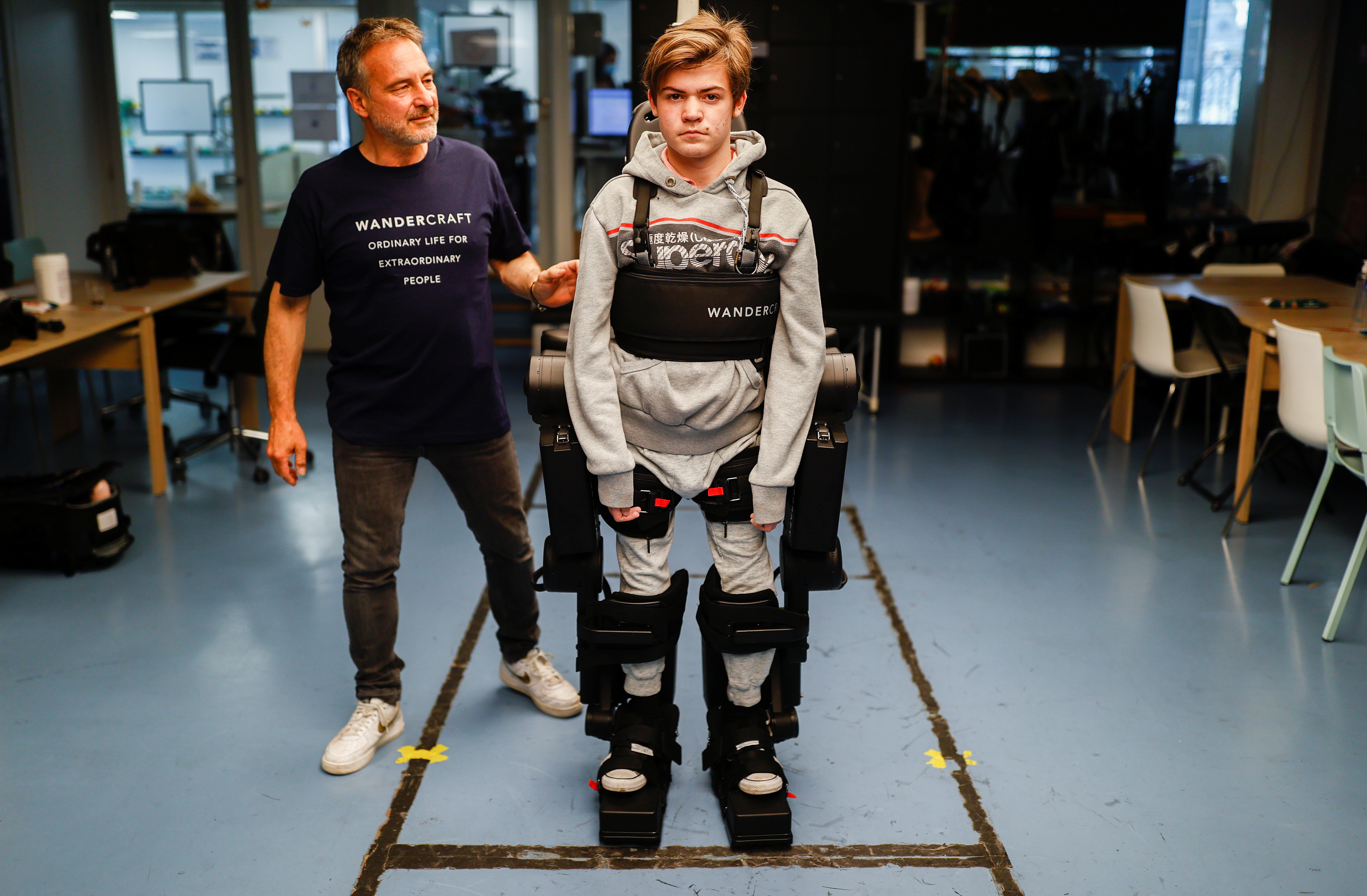 Jean-Louis Constanza, Chief Business and Clinical Officer at French company Wandercraft helps his 16-year-old son Oscar using a robot exoskeleton at the company headquarters in Paris, France July 9, 2021. Picture taken July 9, 2021. REUTERS/Christian Hartmann