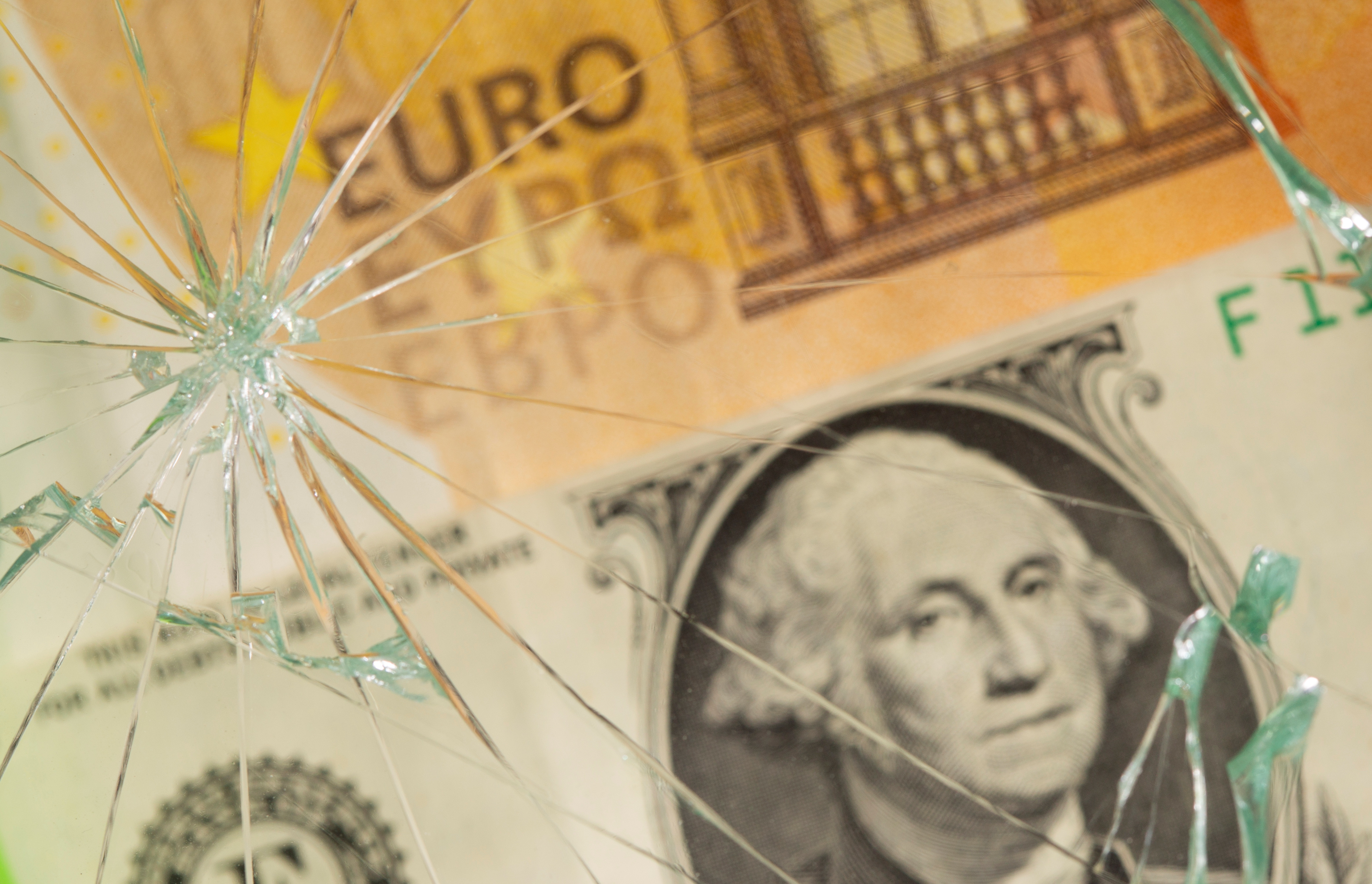 U.S. dollar and euro banknotes are seen through broken glass in this illustration