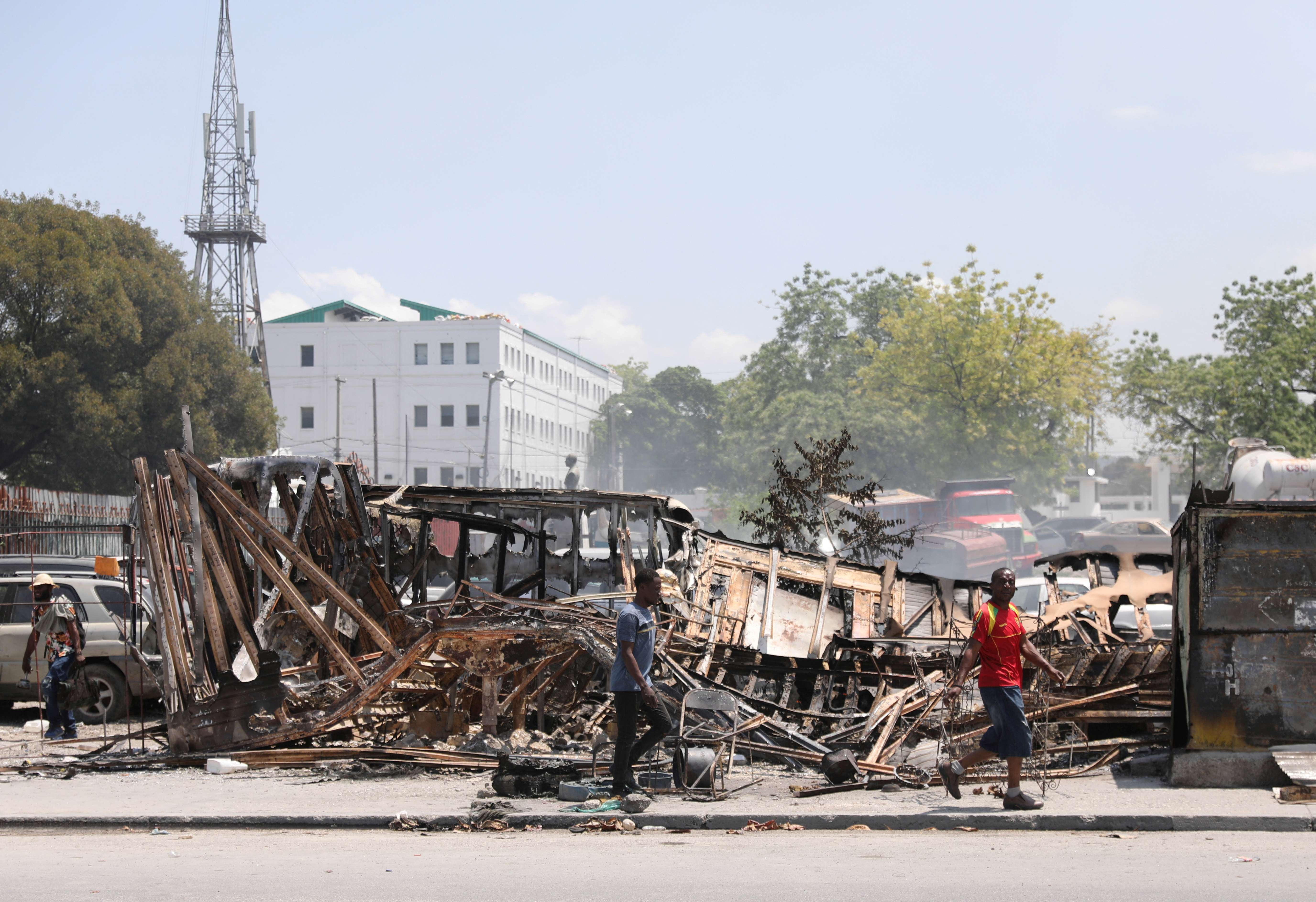 People walk past remains of vehicles after they were set on fire by gangs, in Port-au-Prince