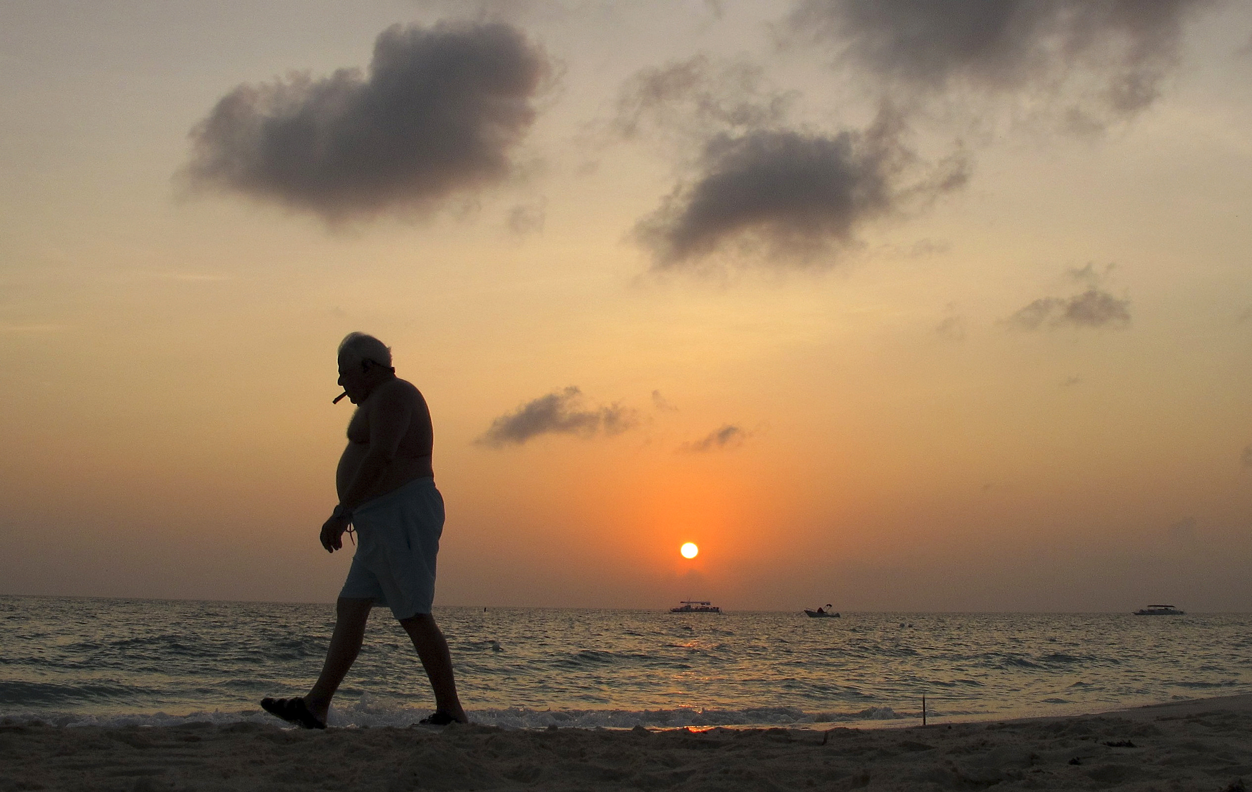 A man smokes a cigar as he walks along Seven Mile Beach in George Town, Cayman Islands
