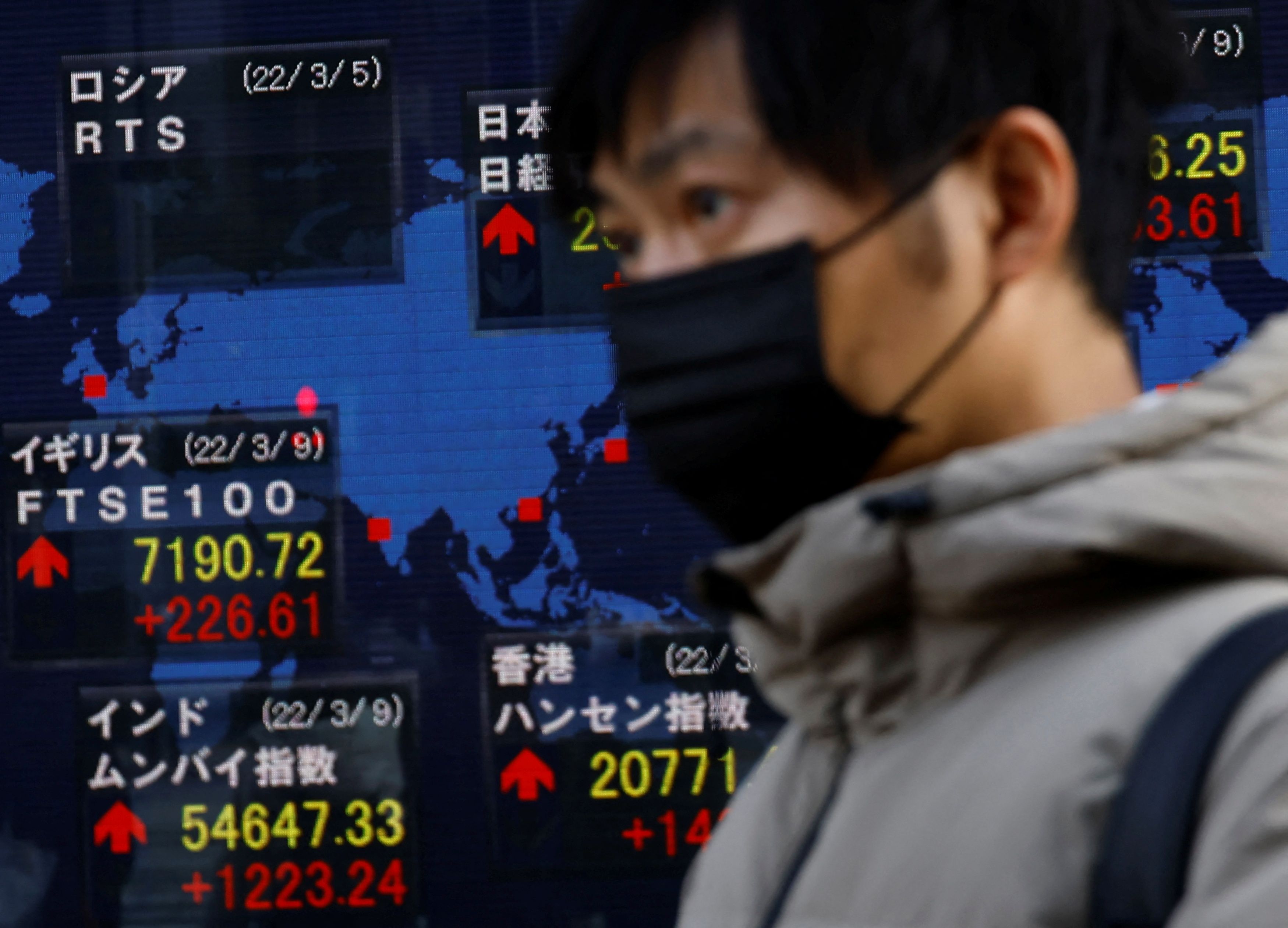 A man wearing a protective mask, amid the coronavirus disease (COVID-19) outbreak, walks past an electronic board displaying various countries' stock indexes including  Russian Trading System (RTS) Index which is empty, outside a brokerage in Tokyo