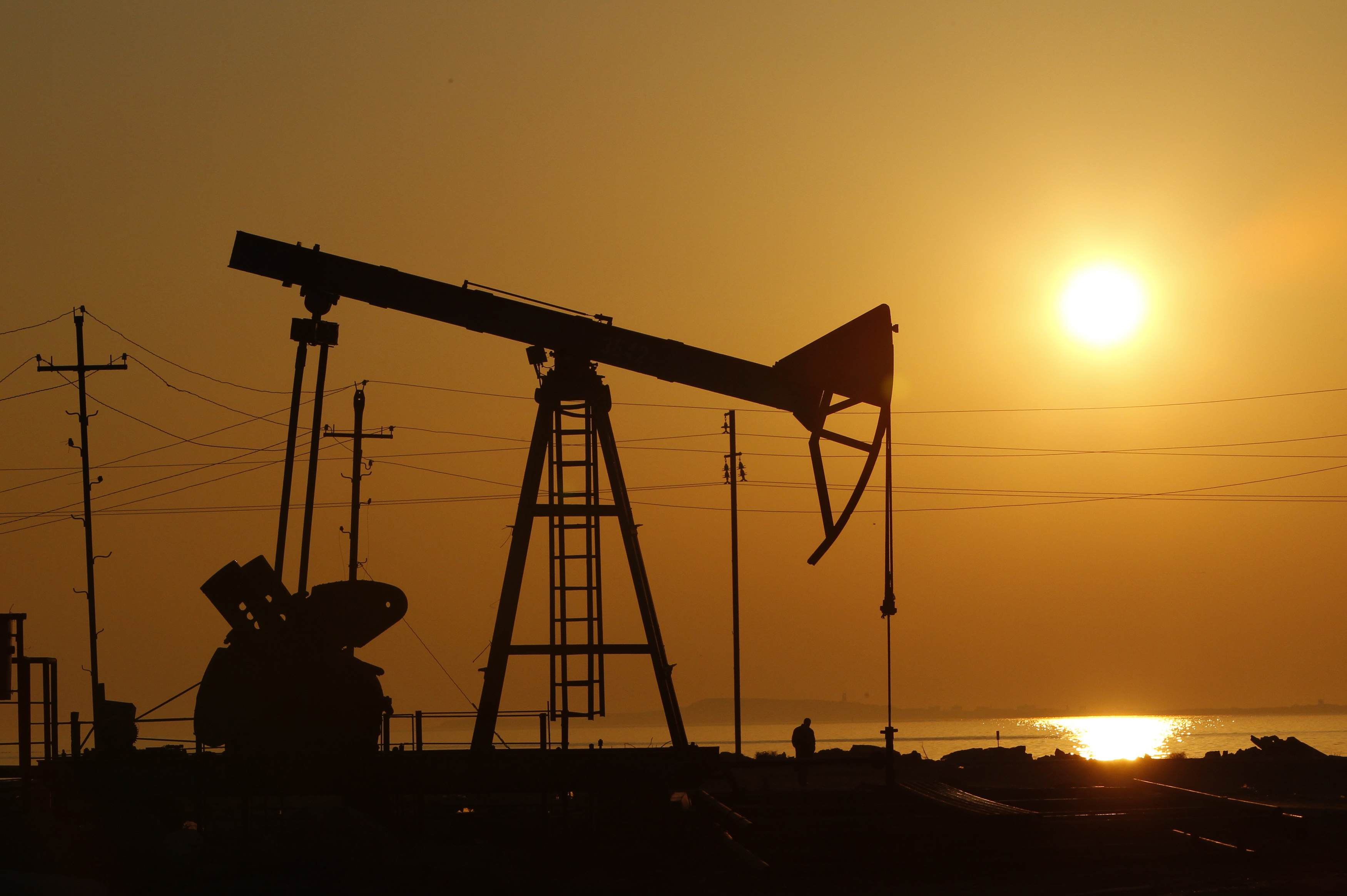 Pump jacks are silhouetted against the rising sun at an oilfield in Baku