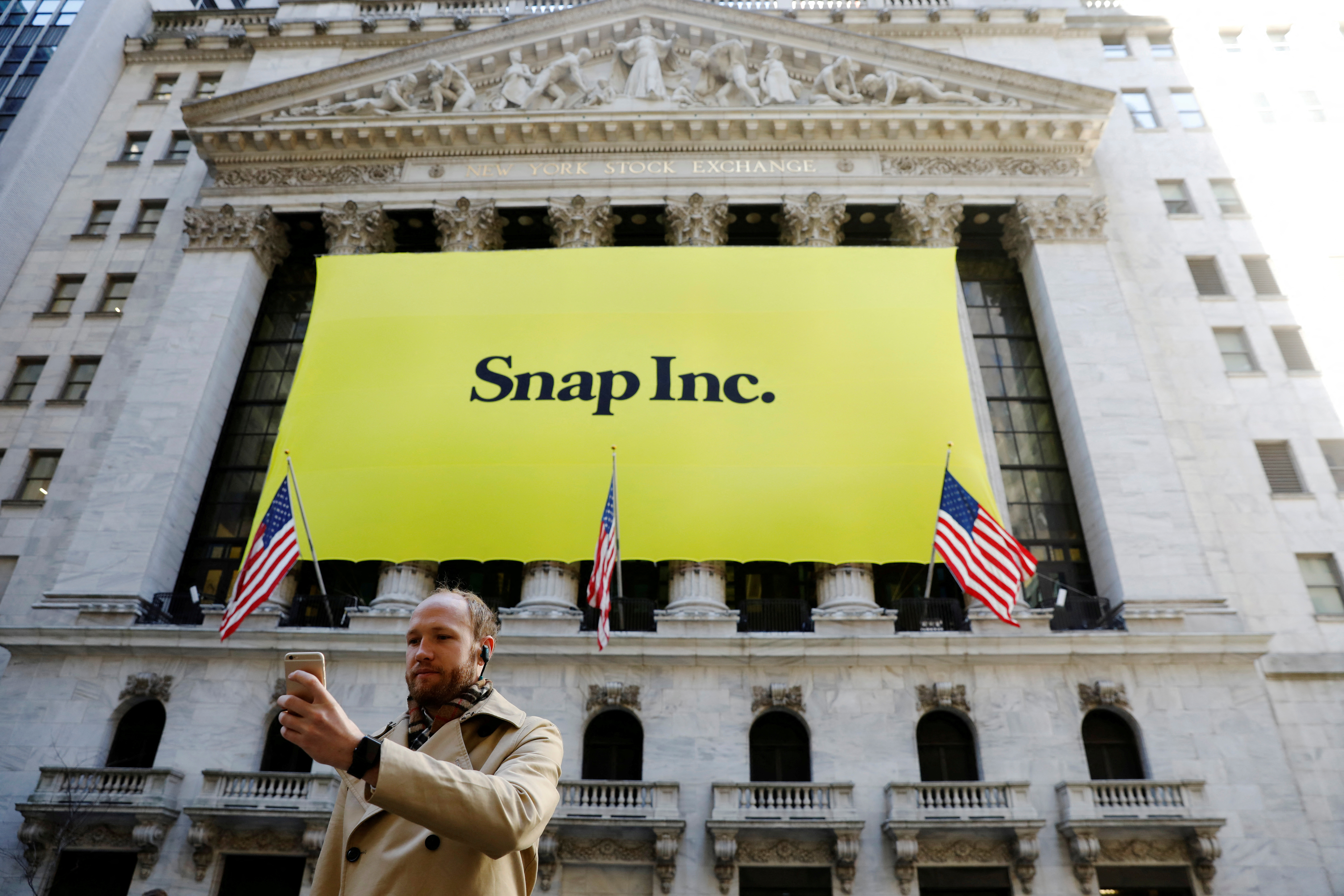  A man takes a photograph of the front of the New York Stock Exchange (NYSE) with a Snap Inc. logo hung on the front of it shortly before the company's IPO in New York, U.S., March 2, 2017. REUTERS/Lucas Jackson/File Photo