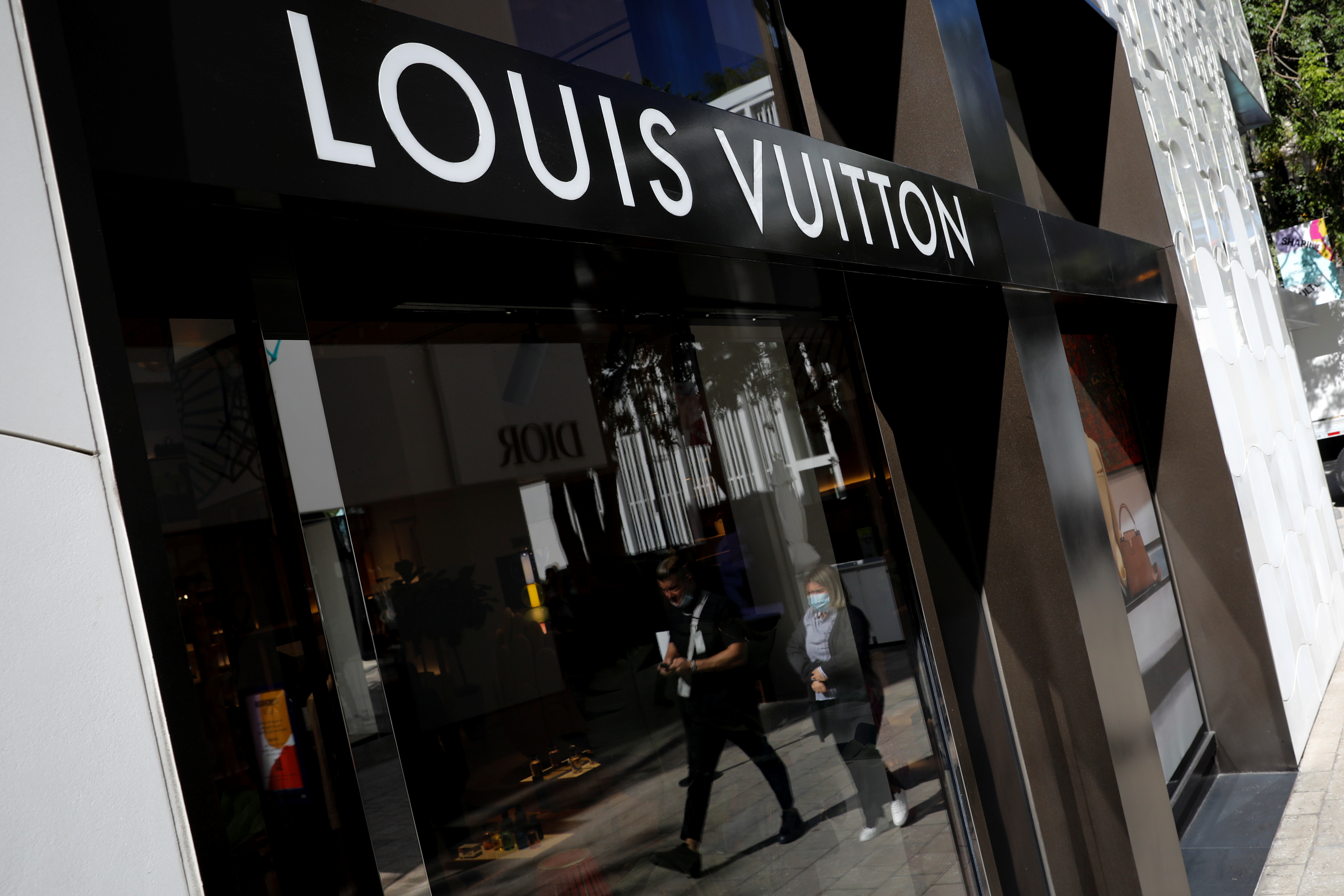 People walk past the Louis Vuitton store at Miami Design District, in Miami