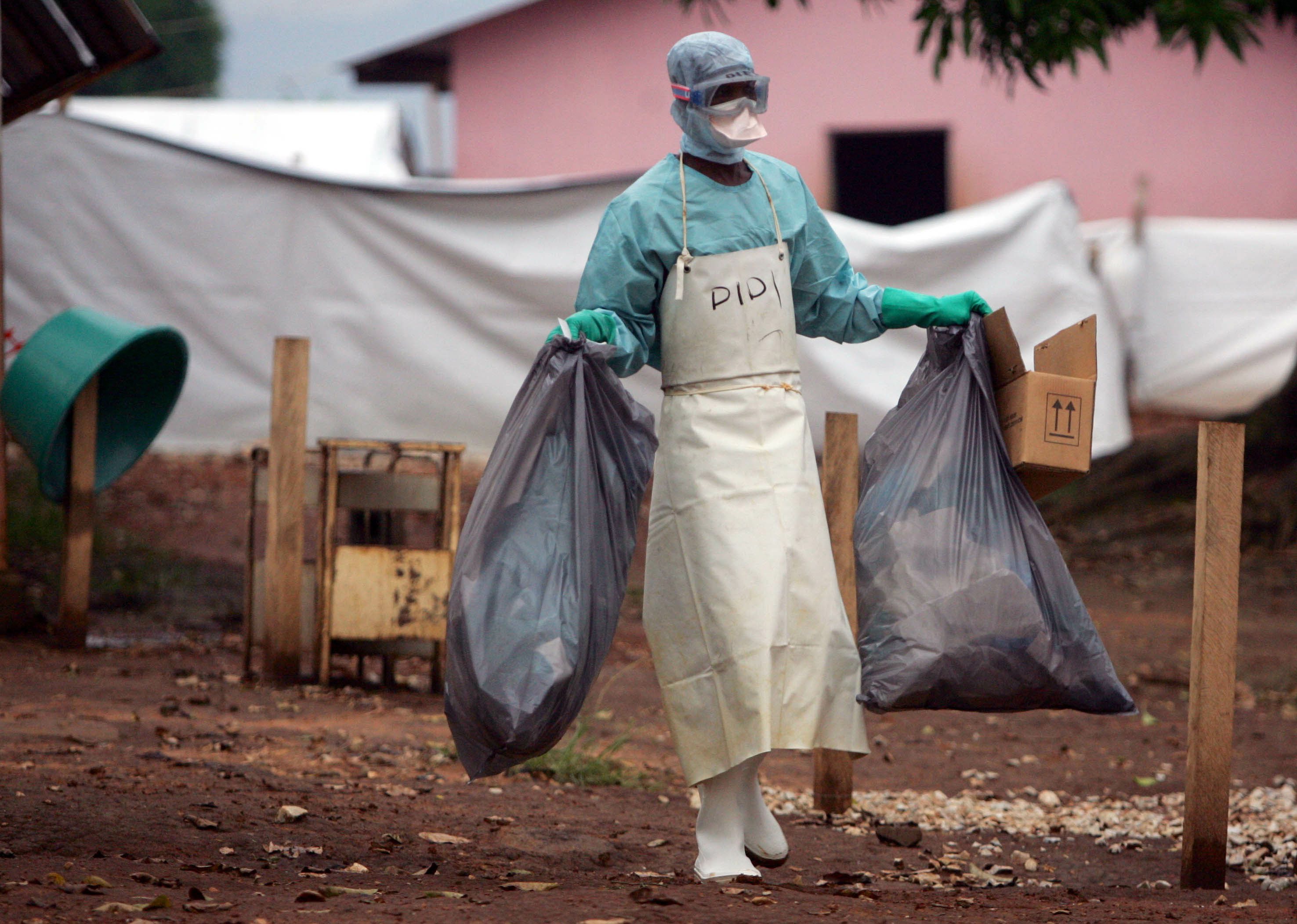 A health worker in protective clothing carries waste for disposal outside the isolation ward where v..