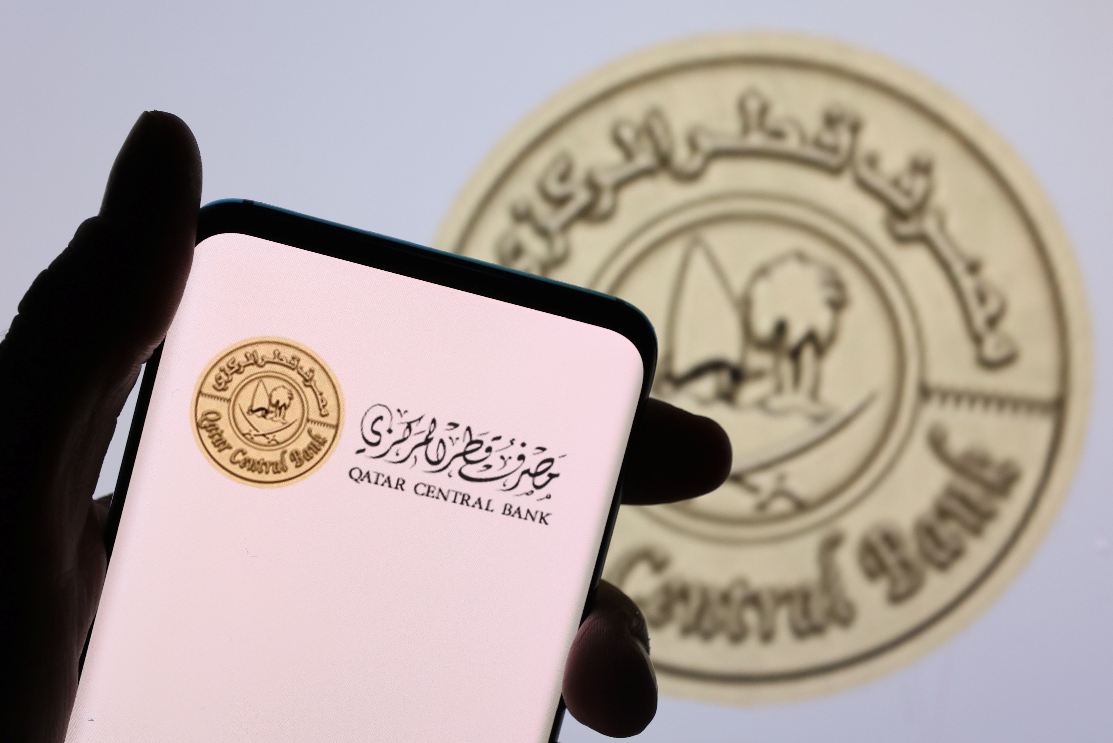 Illustration shows a smartphone with displayed Qatar Central Bank logo