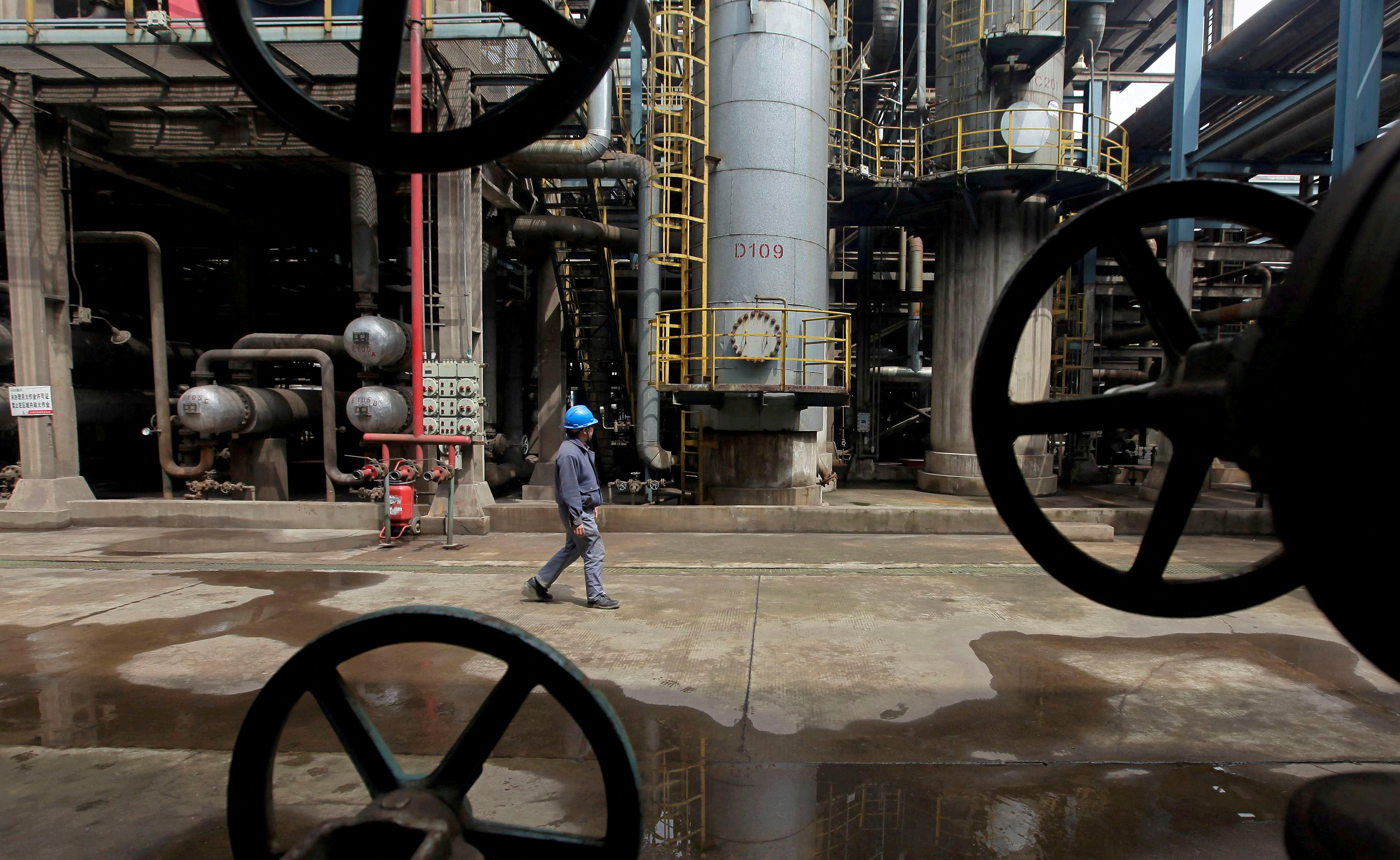 A worker walks past oil pipes at a refinery in Wuhan