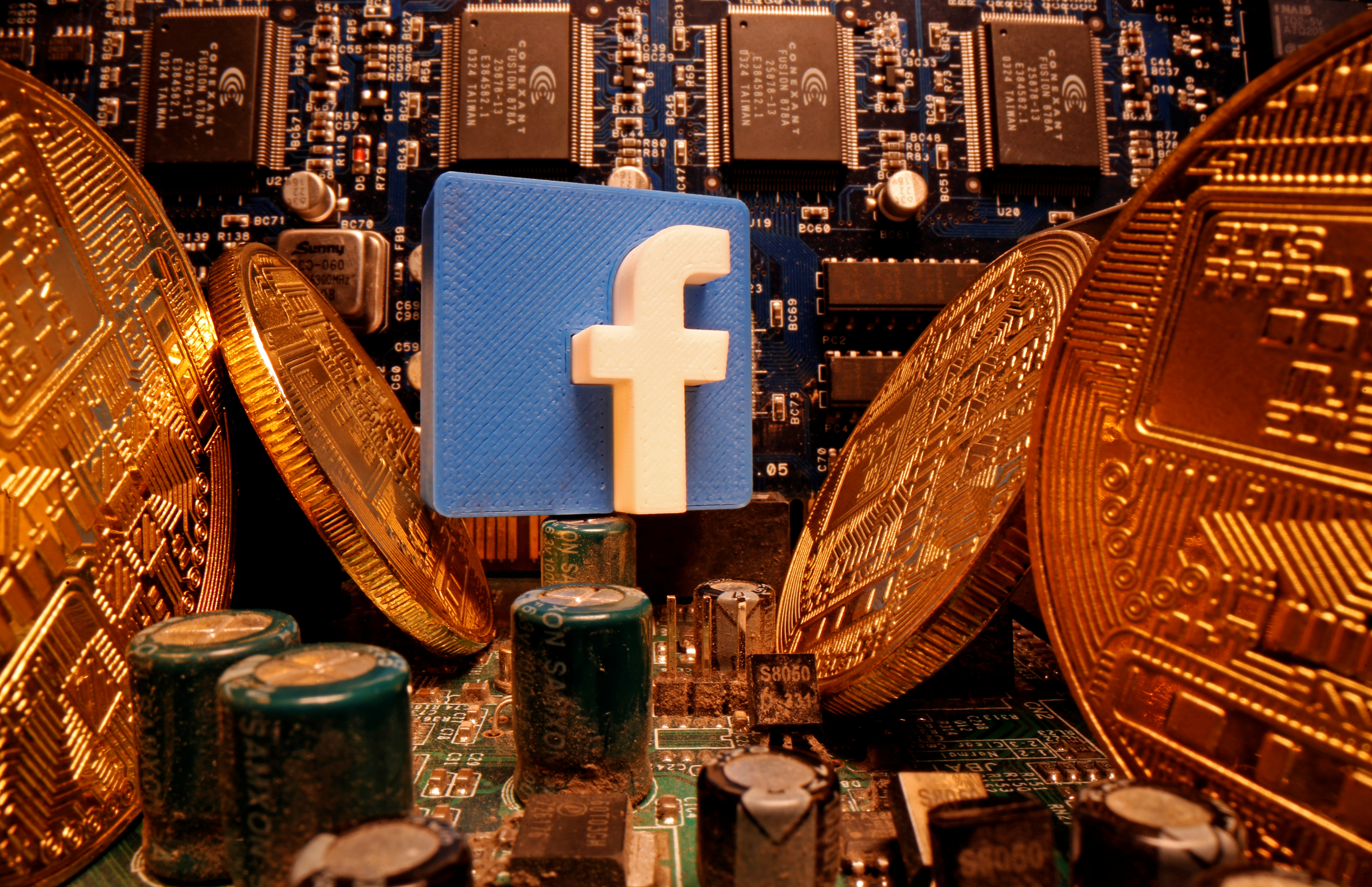 A 3D-printed Facebook logo and representations of cryptocurrency are standing on a motherboard in this picture illustration