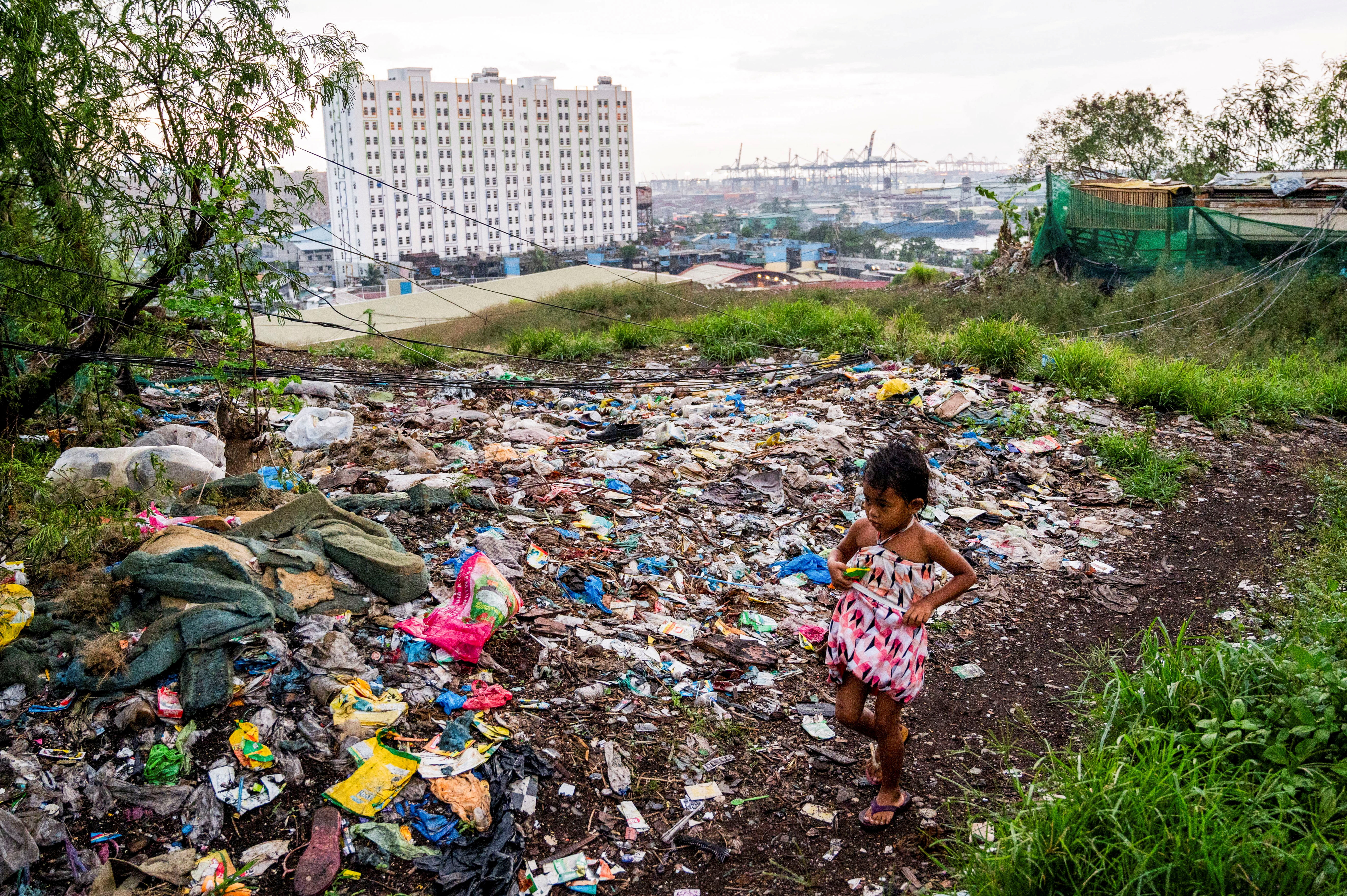 A girl walks past plastic waste dumped at a former landfill in Manila