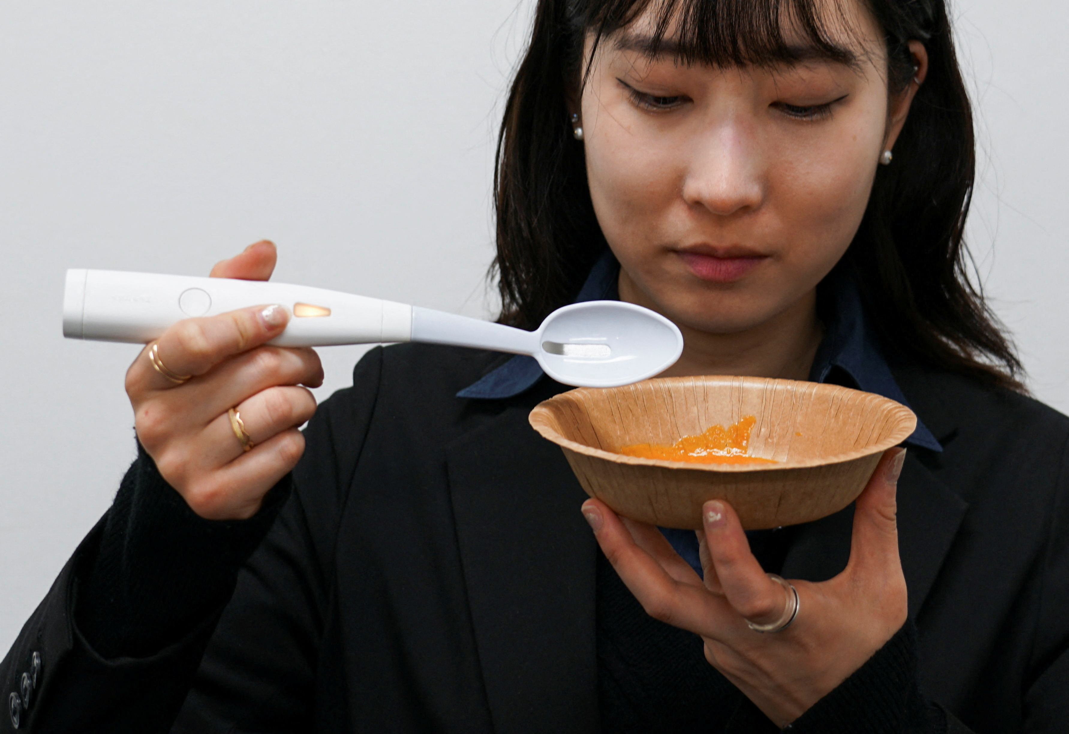An employee of Kirin Holdings demonstrates an electric spoon that can enhance the salty taste in food, in Tokyo