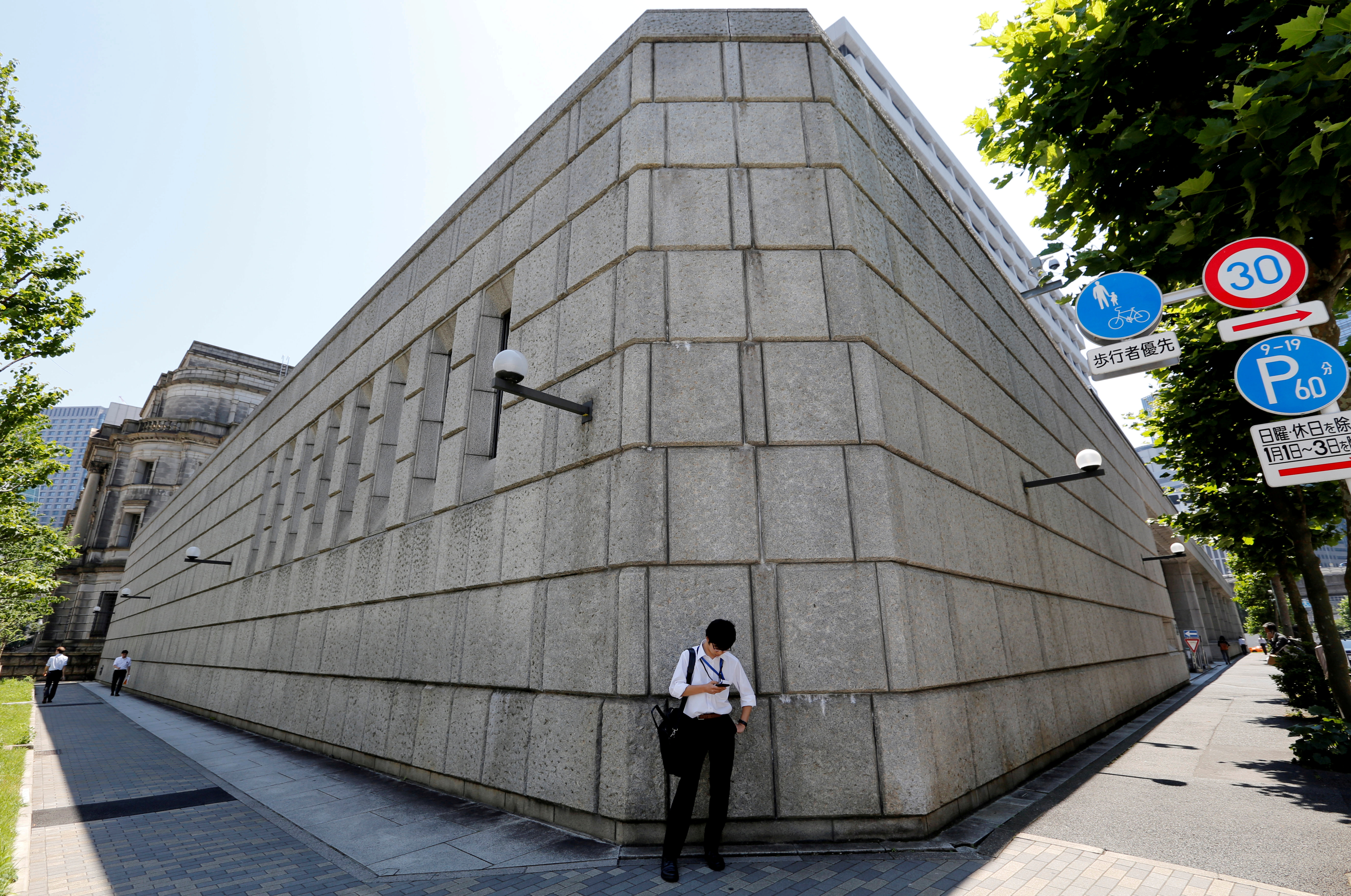 A man looks at a mobile phone in front of the Bank of Japan building in Tokyo