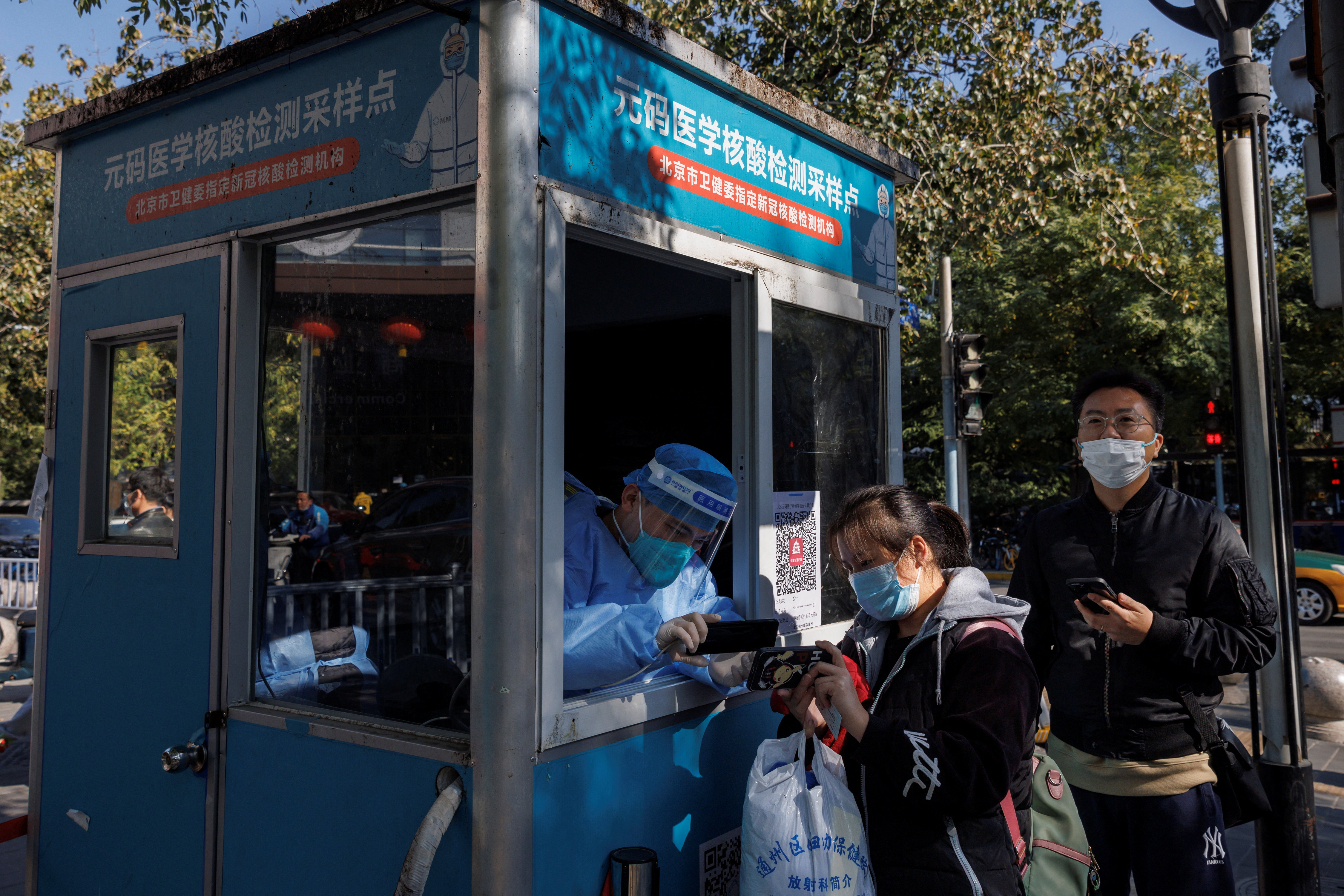 Um trabalhador de prevenção de pandemia registra detalhes pessoais de pessoas enquanto se alinham para fazer testes de swab em uma cabine de teste enquanto surtos de doença por coronavírus (COVID-19) continuam em Pequim