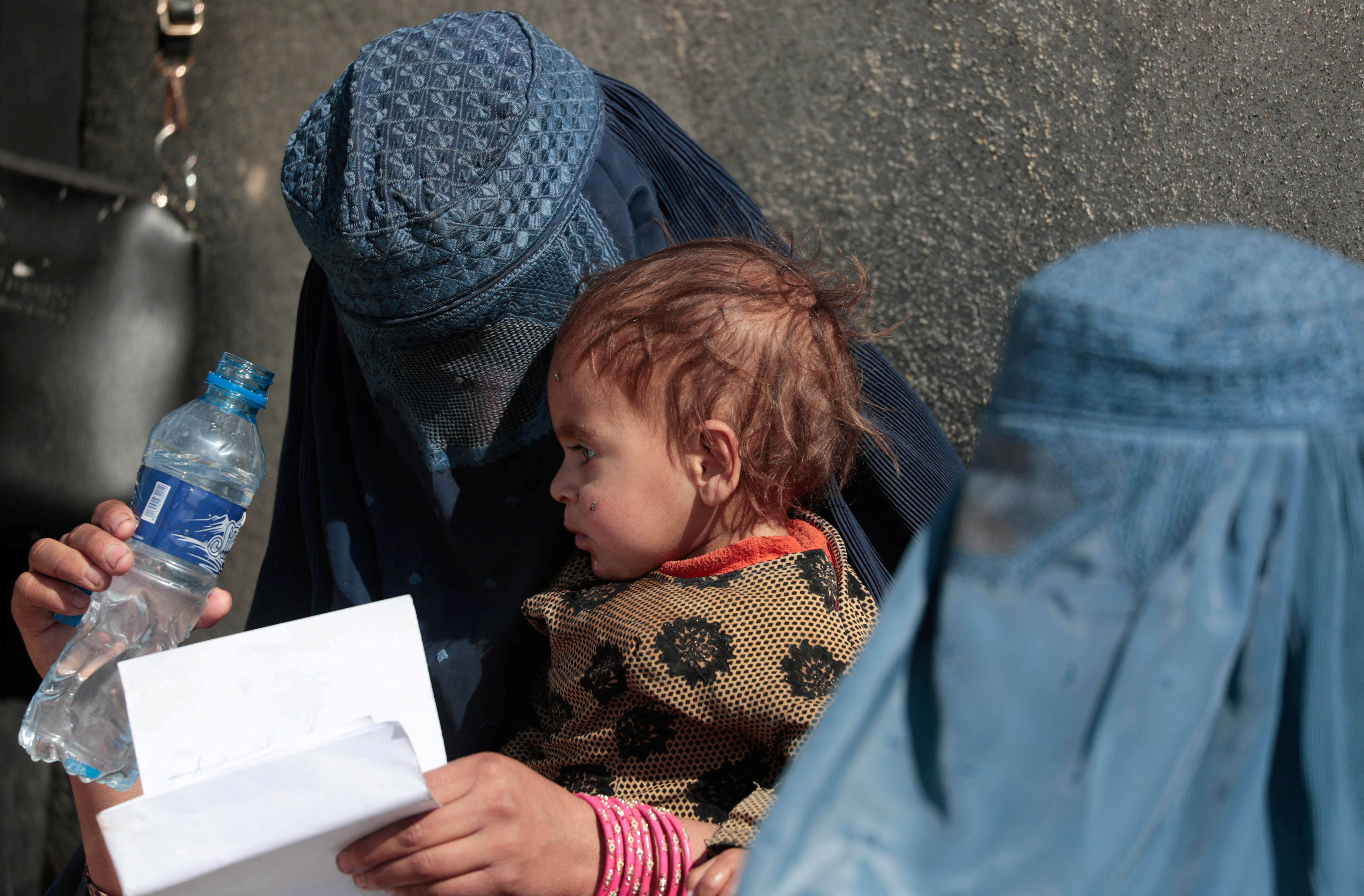 Displaced Afghan woman holds her child as she waits with other women to receive aid supply outside an UNCHR distribution center on the outskirts of Kabul