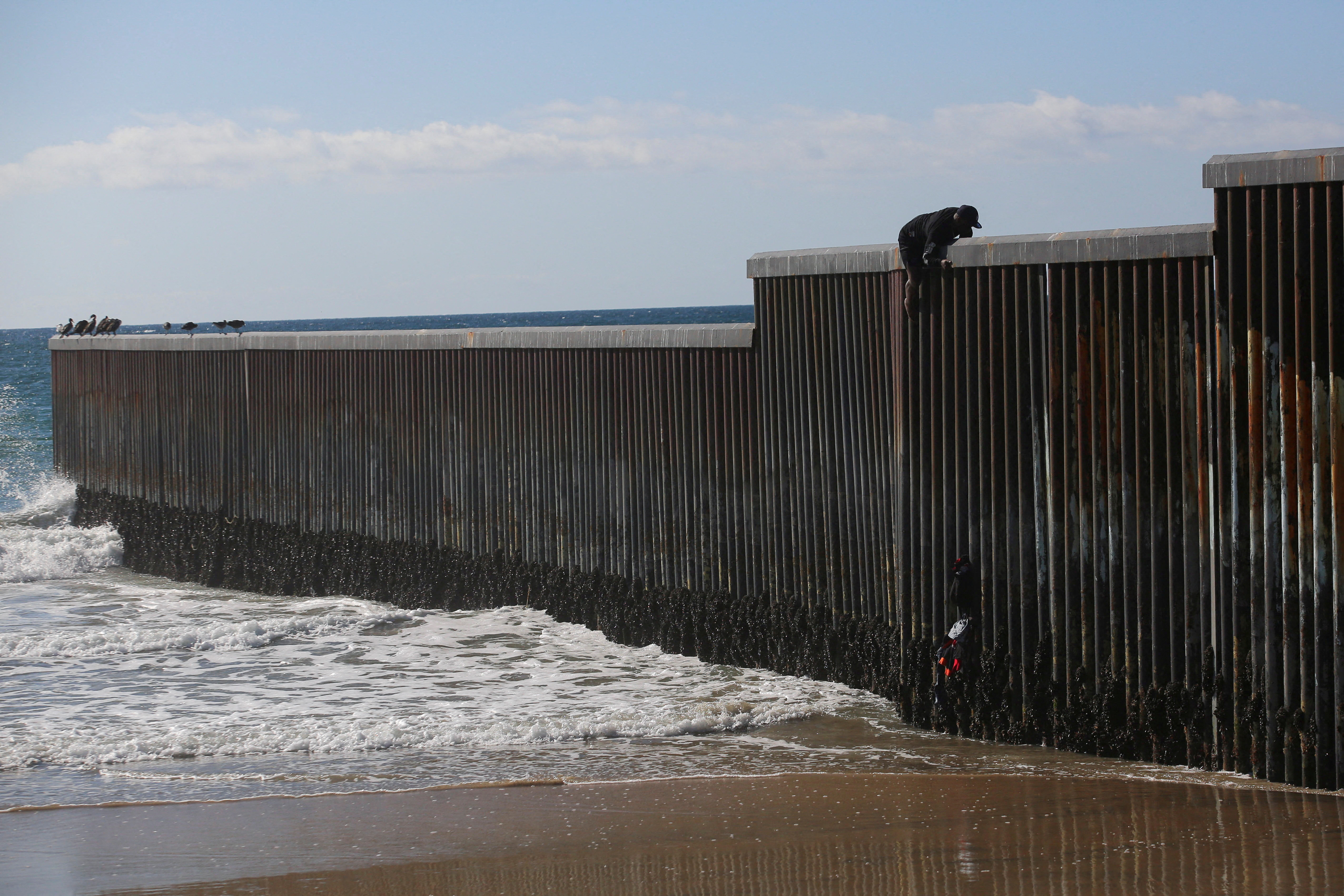 A migrant climbs the border fence to cross into the U.S. to request asylum, in Playas de Tijuana