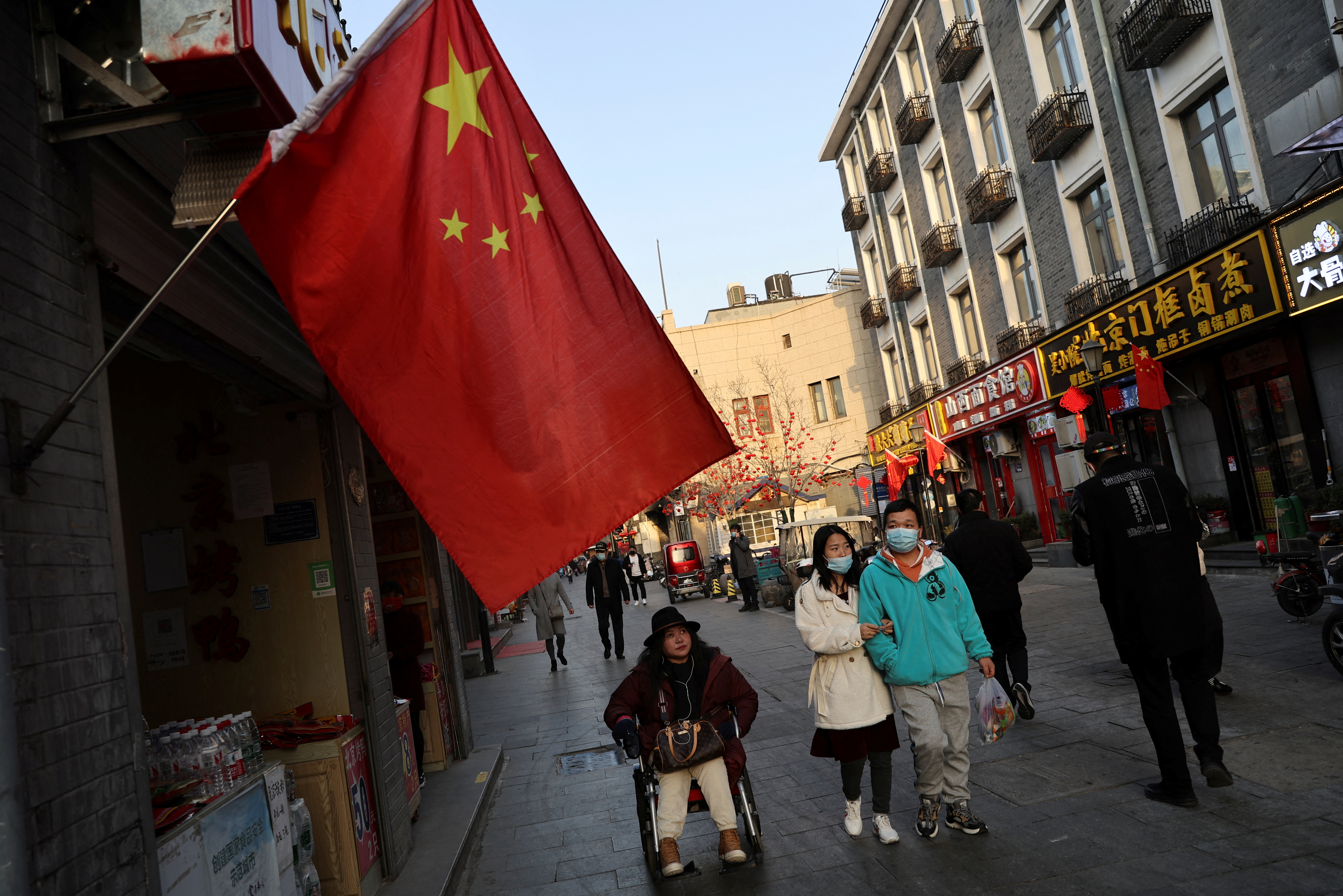 People walk past a shop with a Chinese national flag, ahead of the annual National People's Congress (NPC), on Qianmen Street area, in Beijing