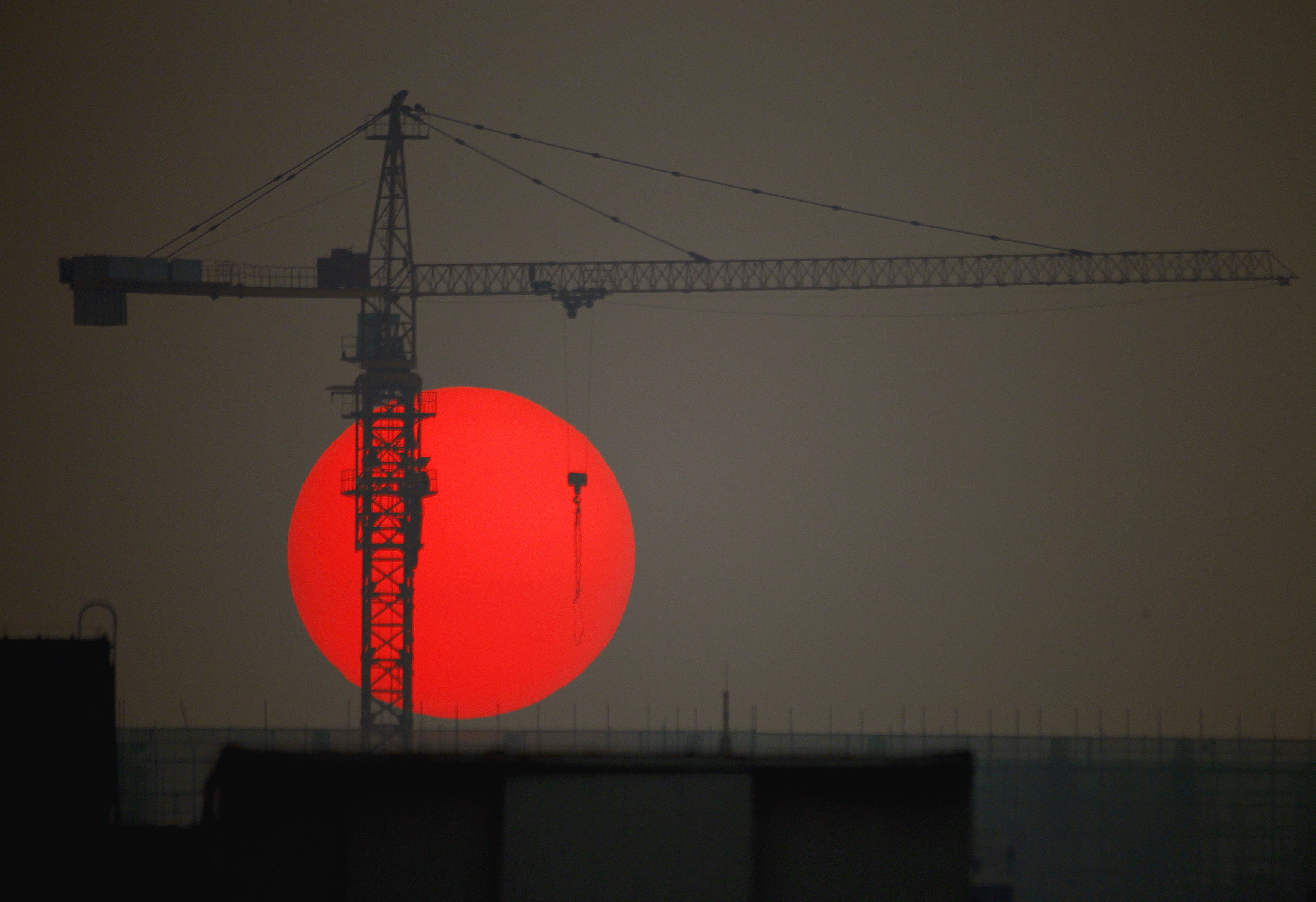 The sun sets behind a crane behind a construction site for a new residential building in central Beijing