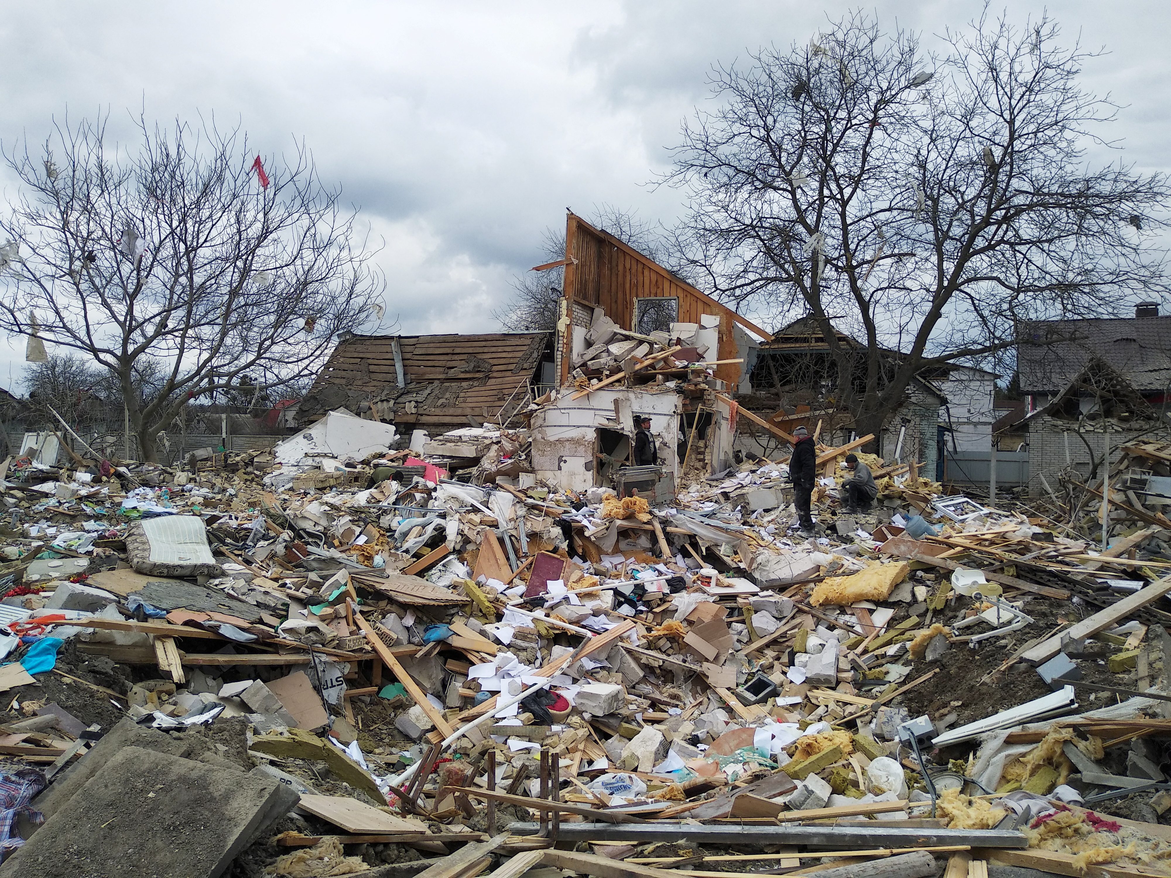People are seen amidst the debris of a house destroyed by shelling in the Kyiv region