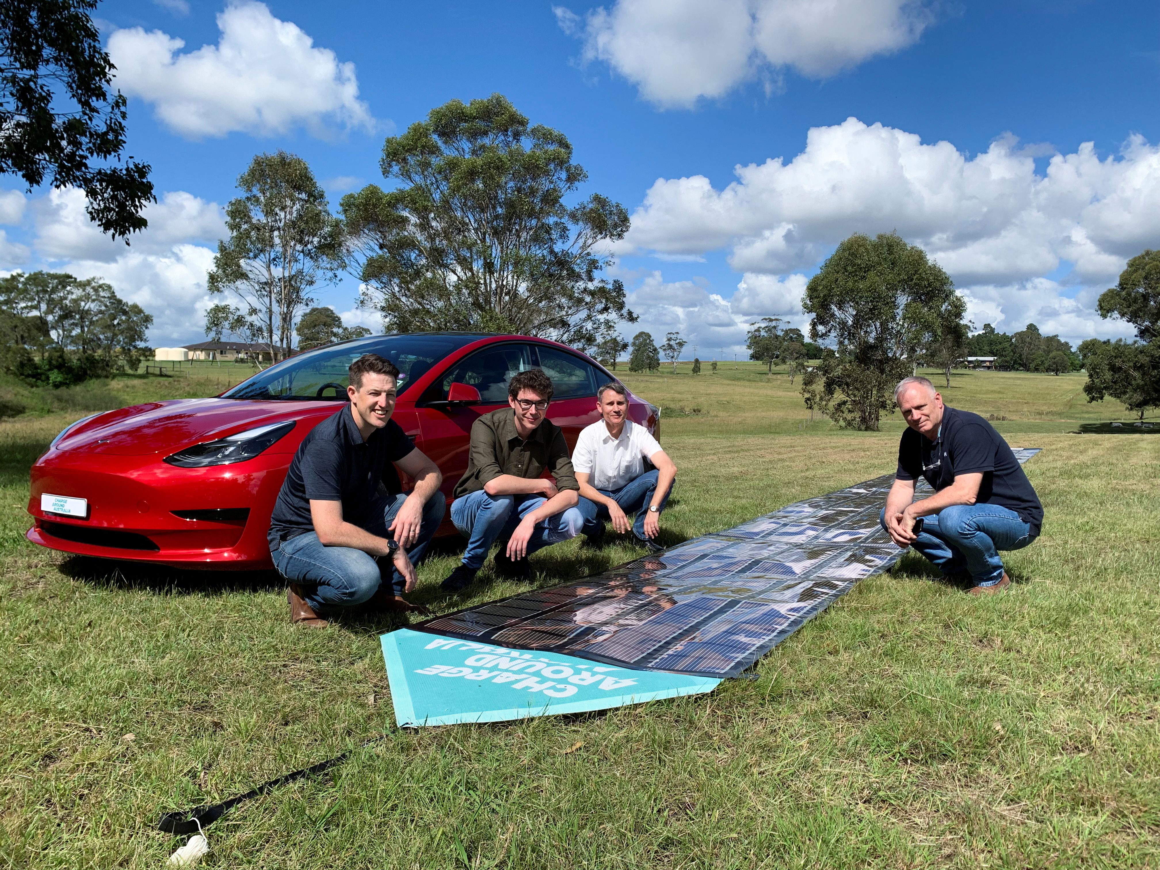 Charge Around Australia project lead and inventor of 'printed solar' panels Paul Dastoor and team members next to a printed solar panel and Tesla car, in Gosforth
