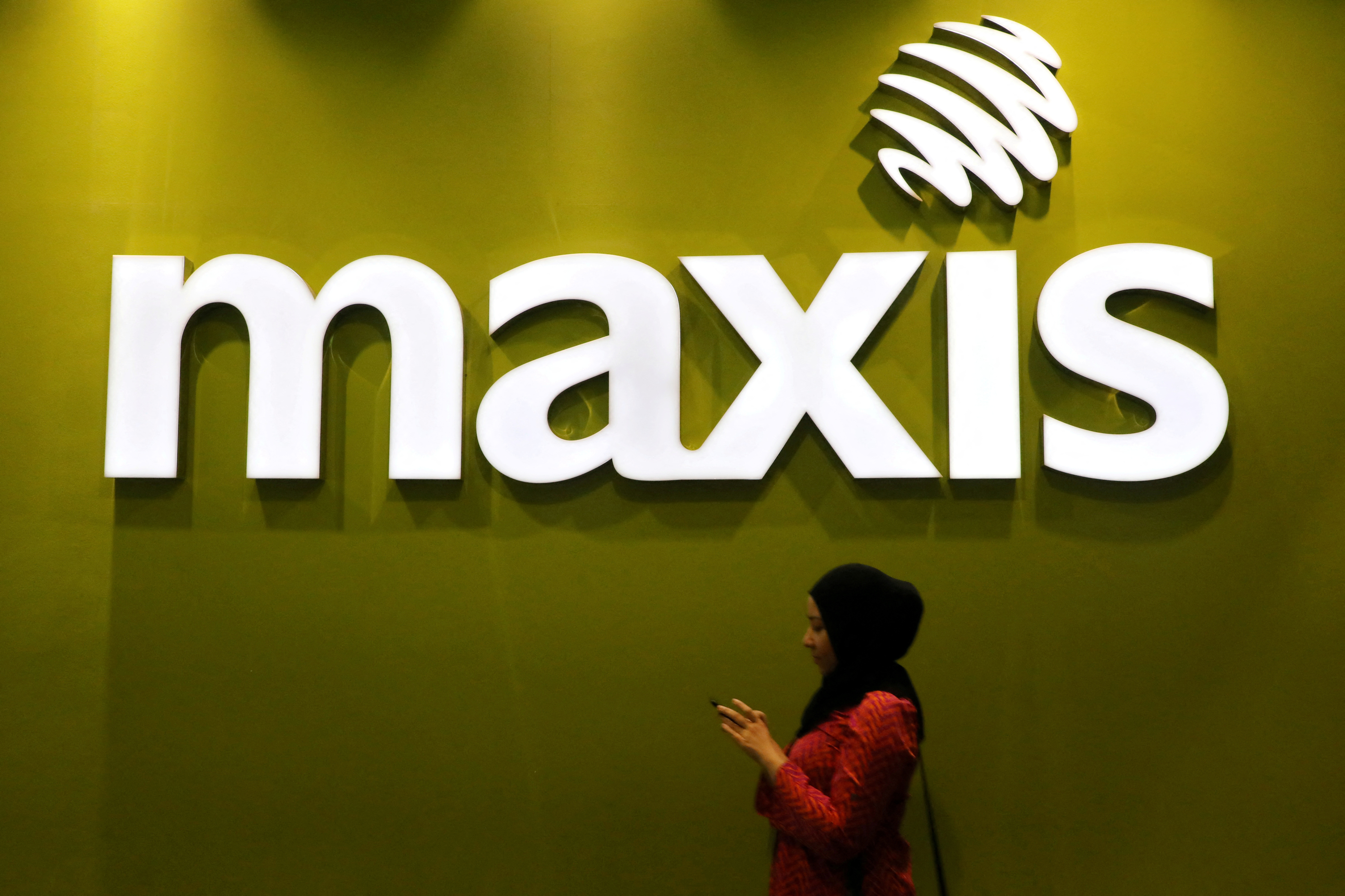 A woman walks past a logo of Maxis at its headquarters in Kuala Lumpur