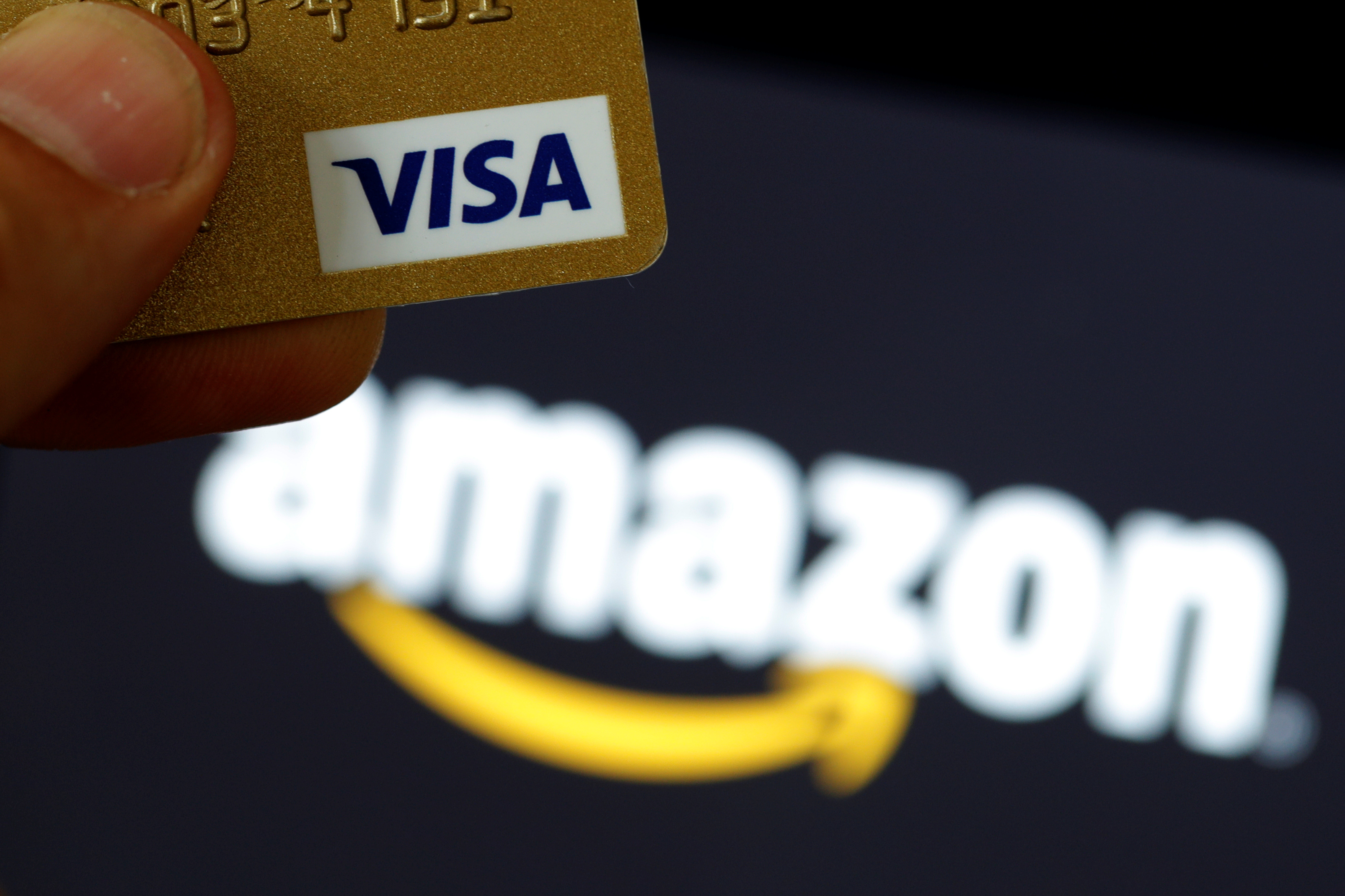 A visa credit card is held in front of an Amazon logo in this picture illustration