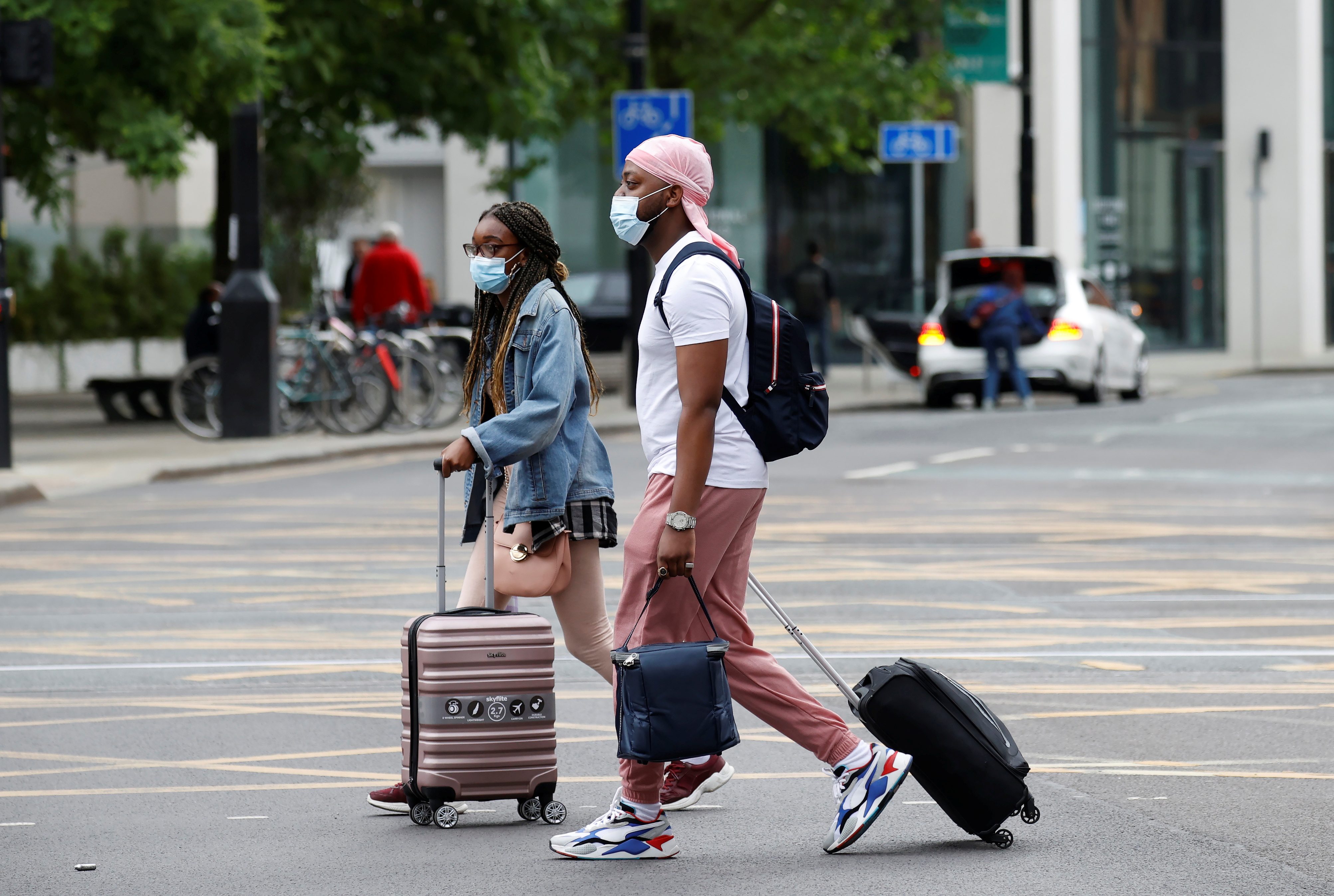 People wear protective masks as they walk with suitcases through the city centre, amid the outbreak of the coronavirus disease (COVID-19) in Manchester
