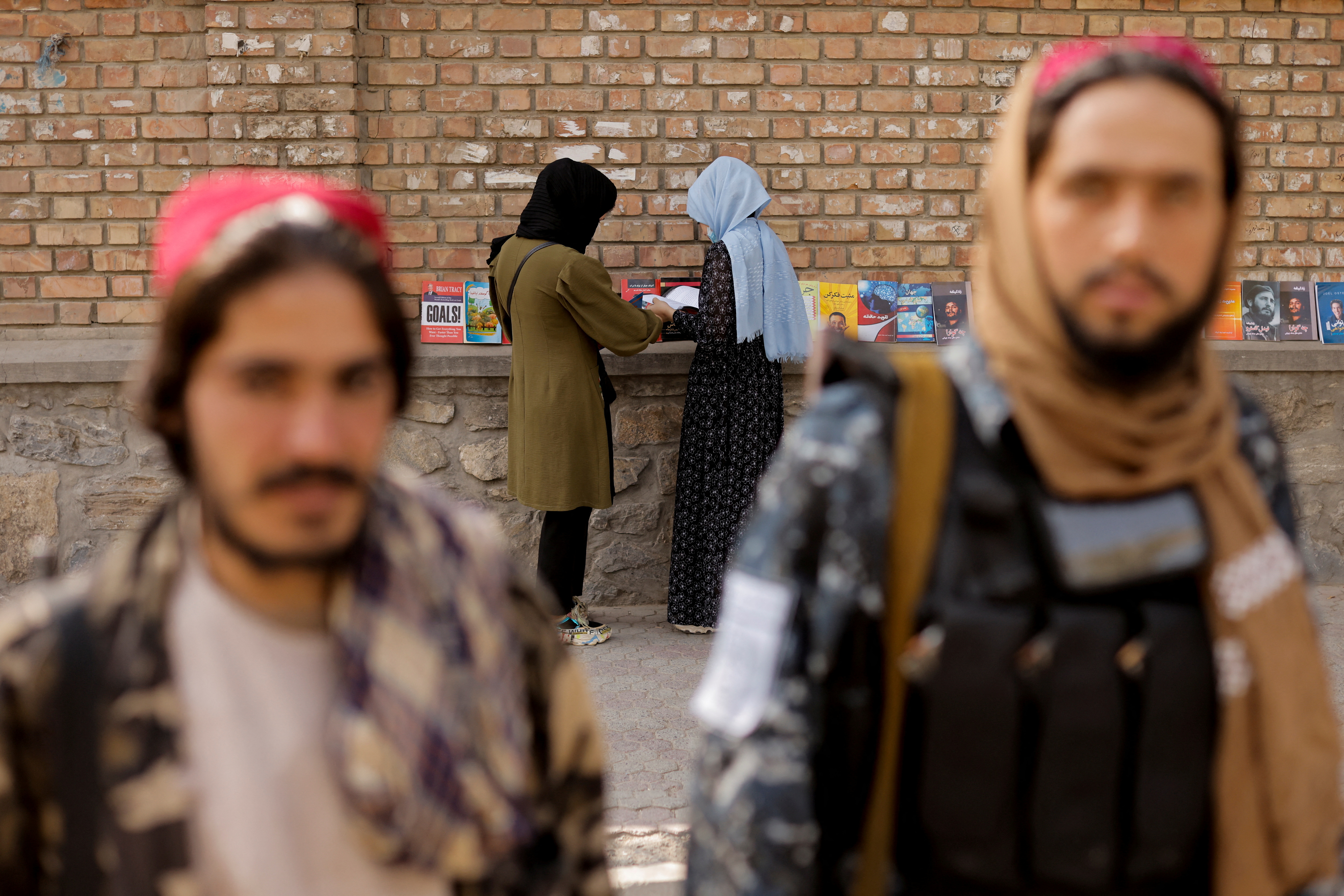 Two girls search for books in a book stall outside the Kabul university while two Taliban soldiers pose in Kabul