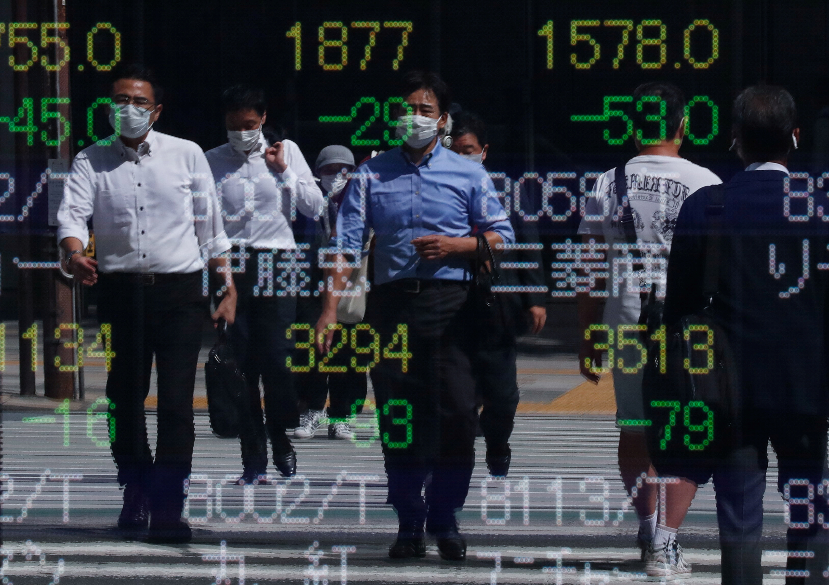 Passersby wearing protective masks are reflected on an electronic board displaying stock prices outside a brokerage amid the coronavirus disease (COVID-19) outbreak, in Tokyo, Japan, September 29, 2021. REUTERS/Issei Kato