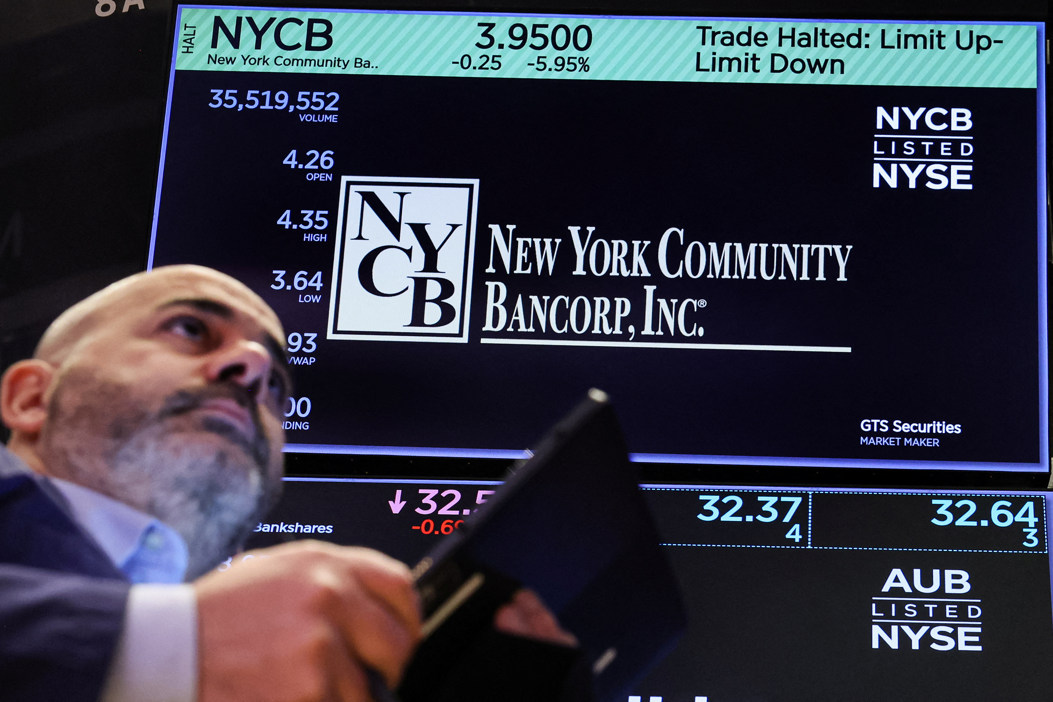 A trader works at the post where New York Community Bancorp stock is traded on the floor at the NYSE in New York