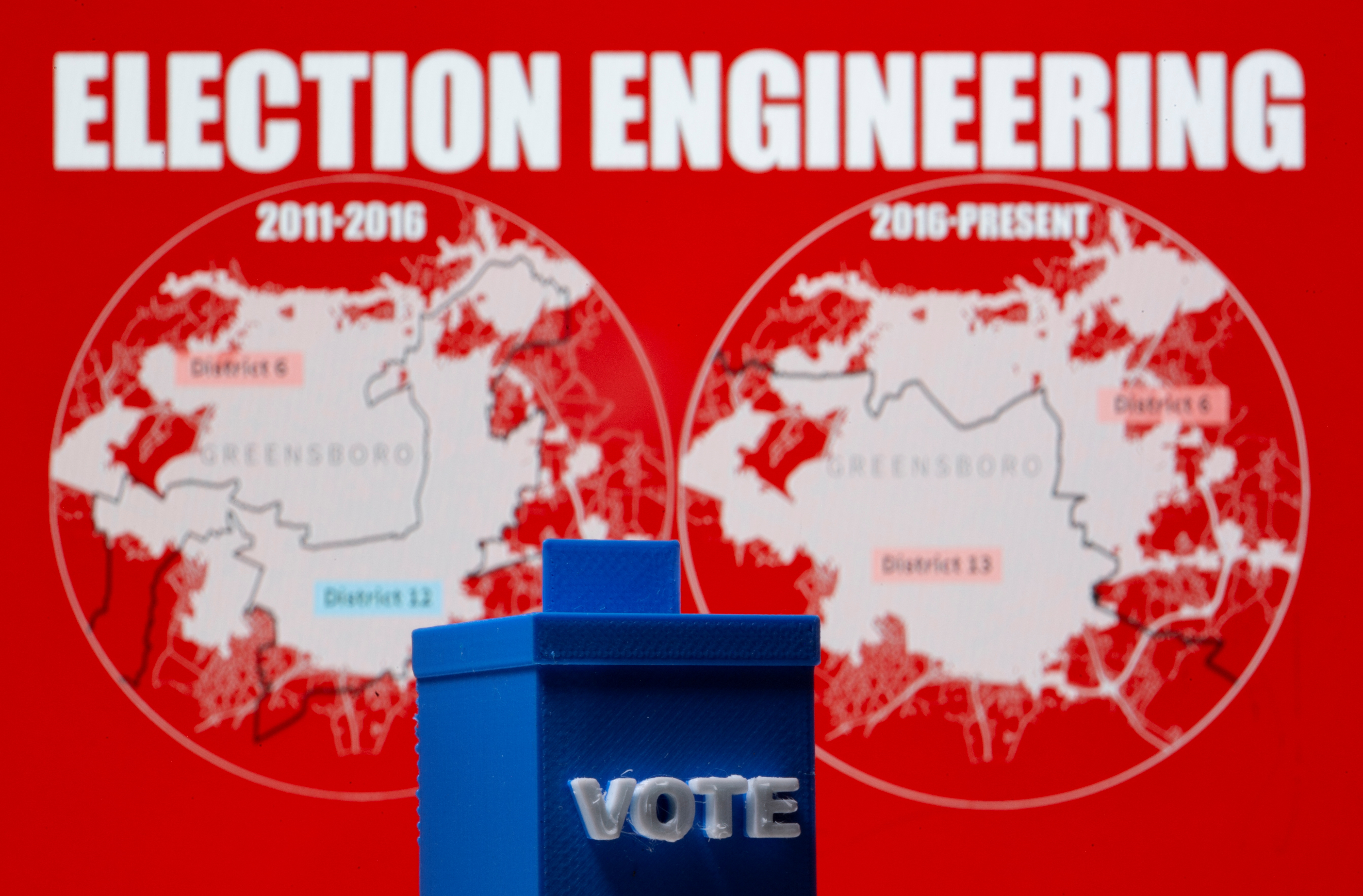 A 3D printed ballot box is seen in front of displayed North Carolina district maps in this illustration