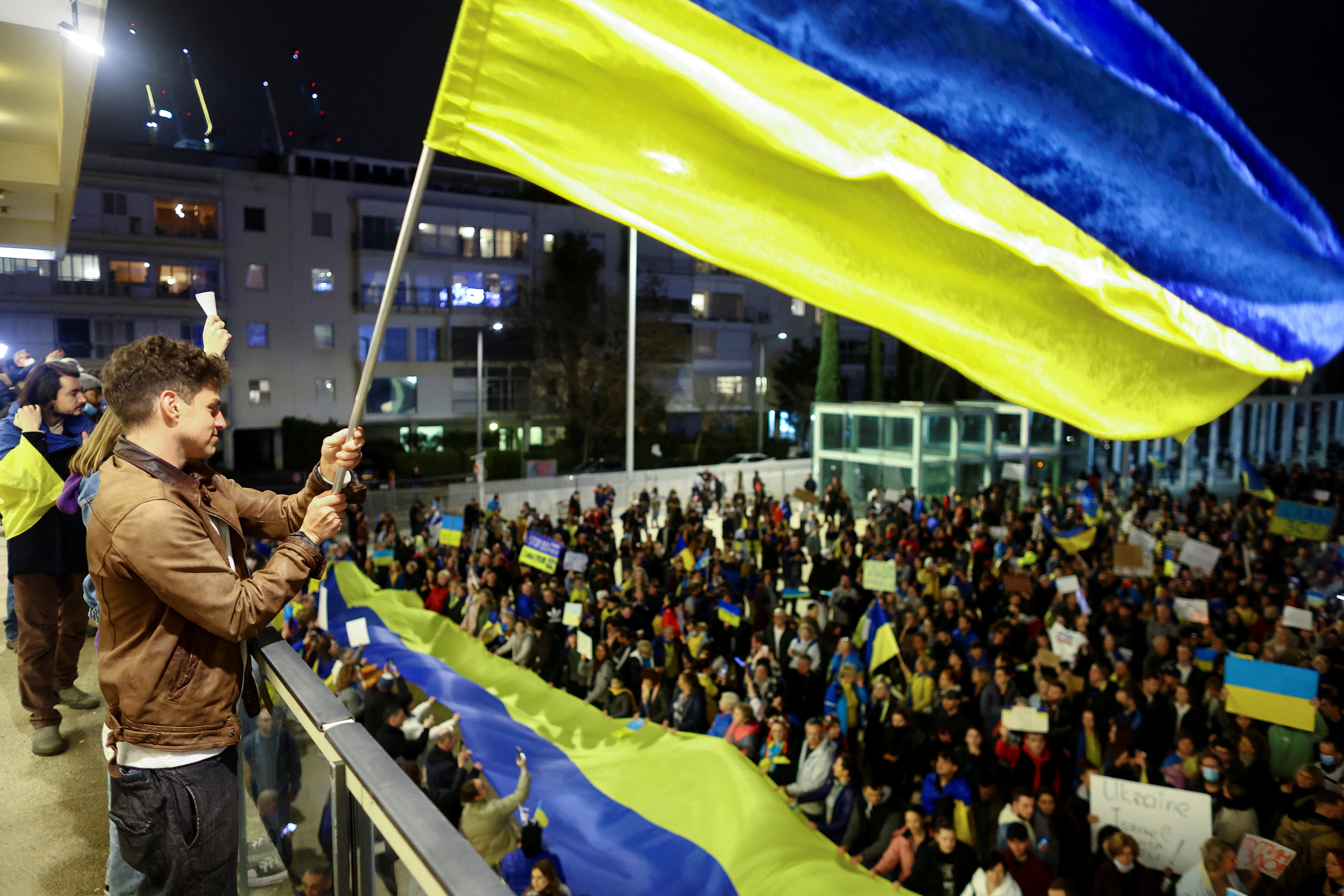 A man waves a flag from a balcony in front of demonstrators attending a rally in support of Ukraine, after Russia launched a massive military operation against Ukraine, in Tel Aviv, Israel