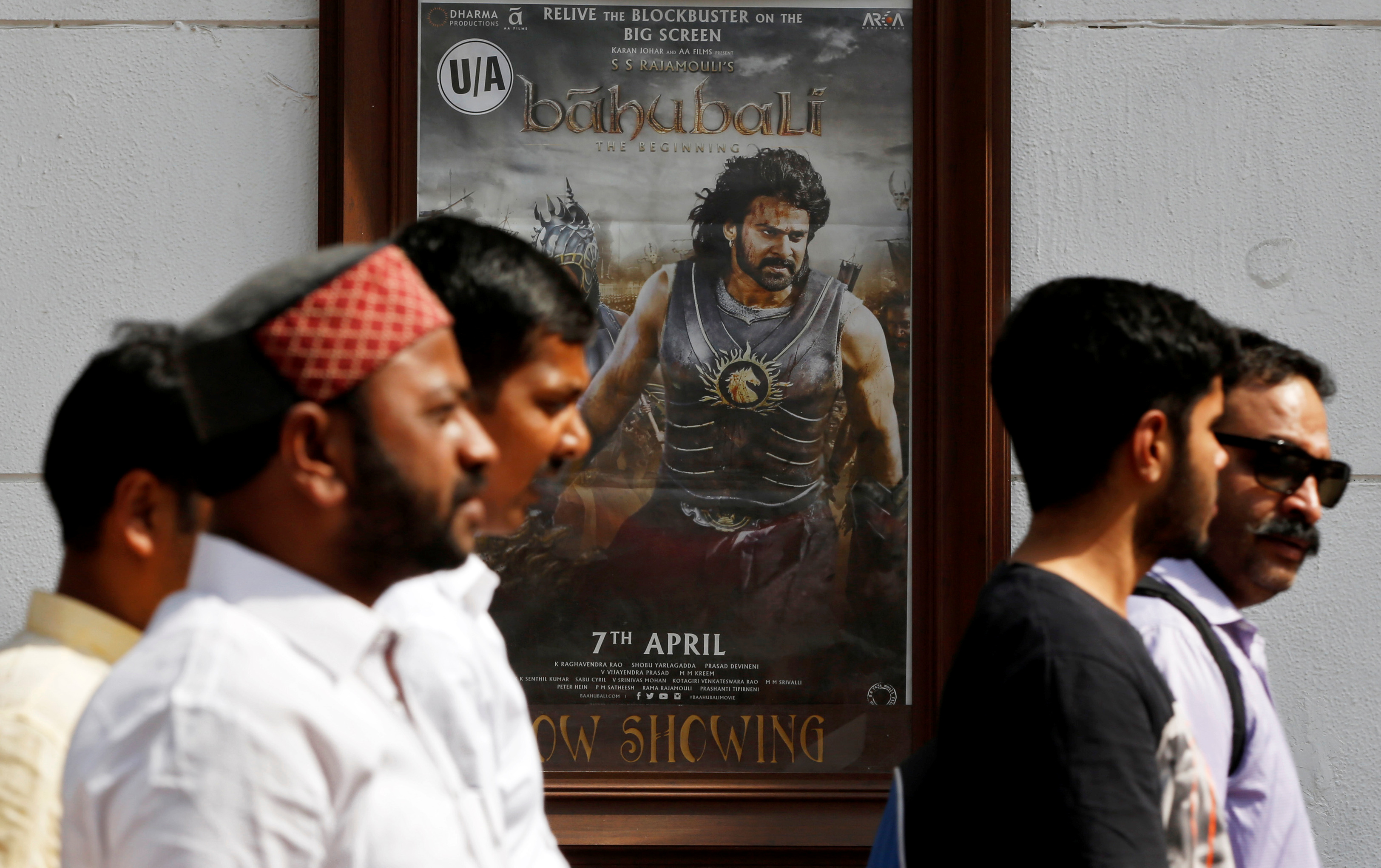 People walk past a poster of an Indian movie 