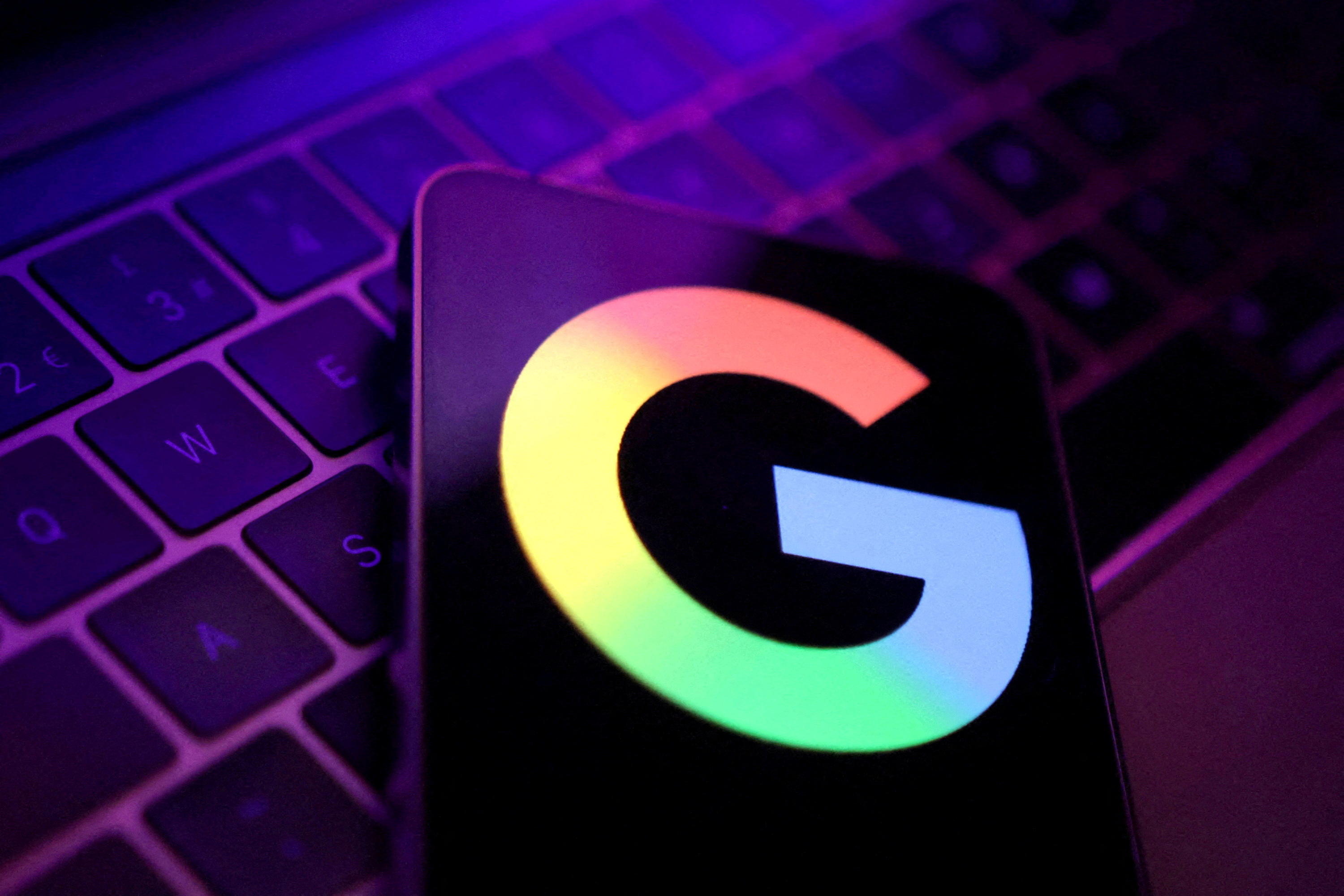 Логотип Google на фоне клавиатуры ноутбука с фиолетовой подсветкой.